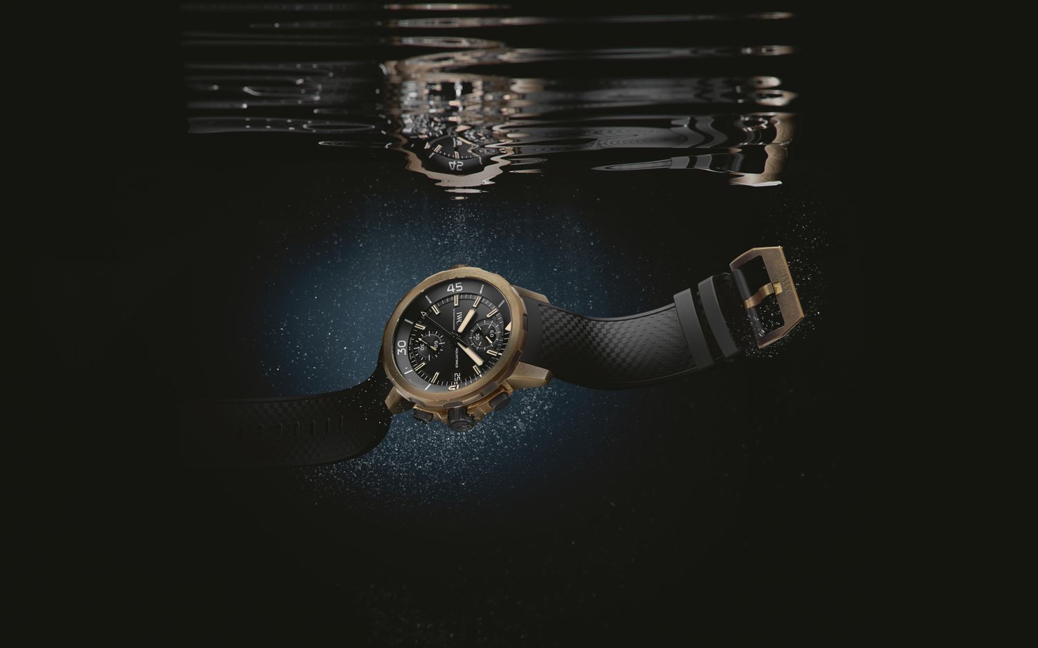 A IWC Schaffhausen Aquatimer with bronze case and black rubber strap beneath the water surface, with reflection and dark background