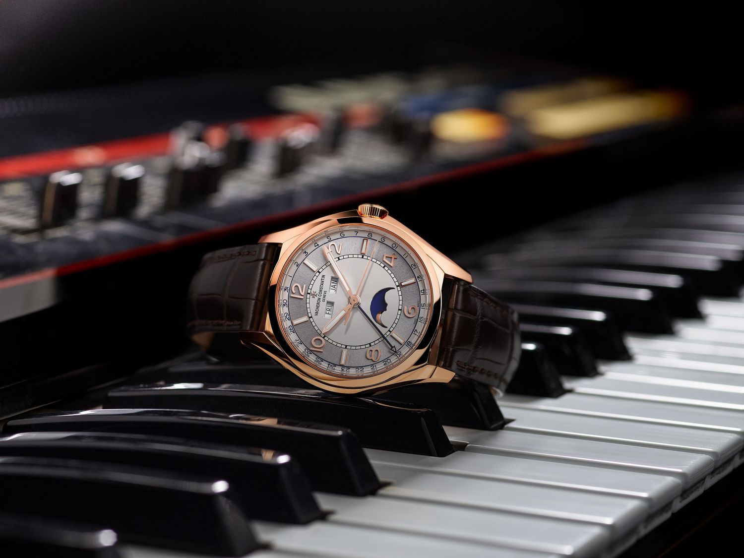 Watch from the Fiftysix collection with moon phase, date and weekday display, staged on a piano.
