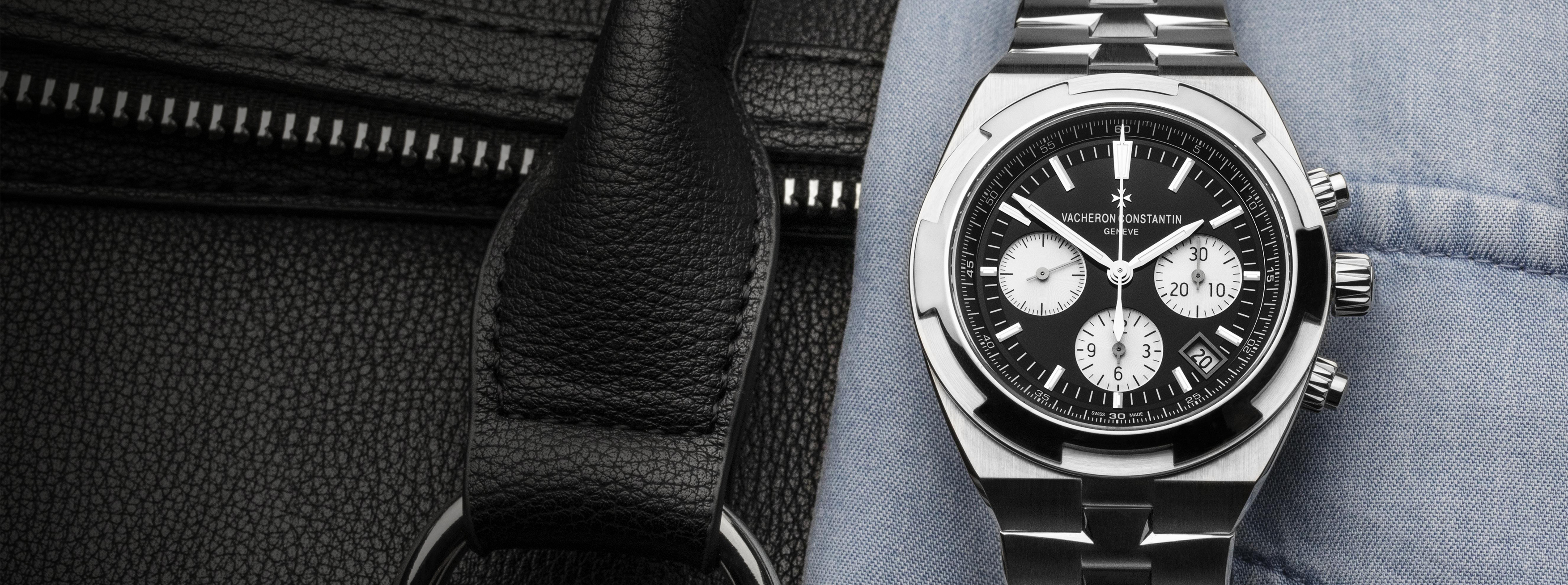 Luxury Vacheron Constantin Overseas chronograph watch with black dial and steel bracelet, placed on leather and fabric accessories.