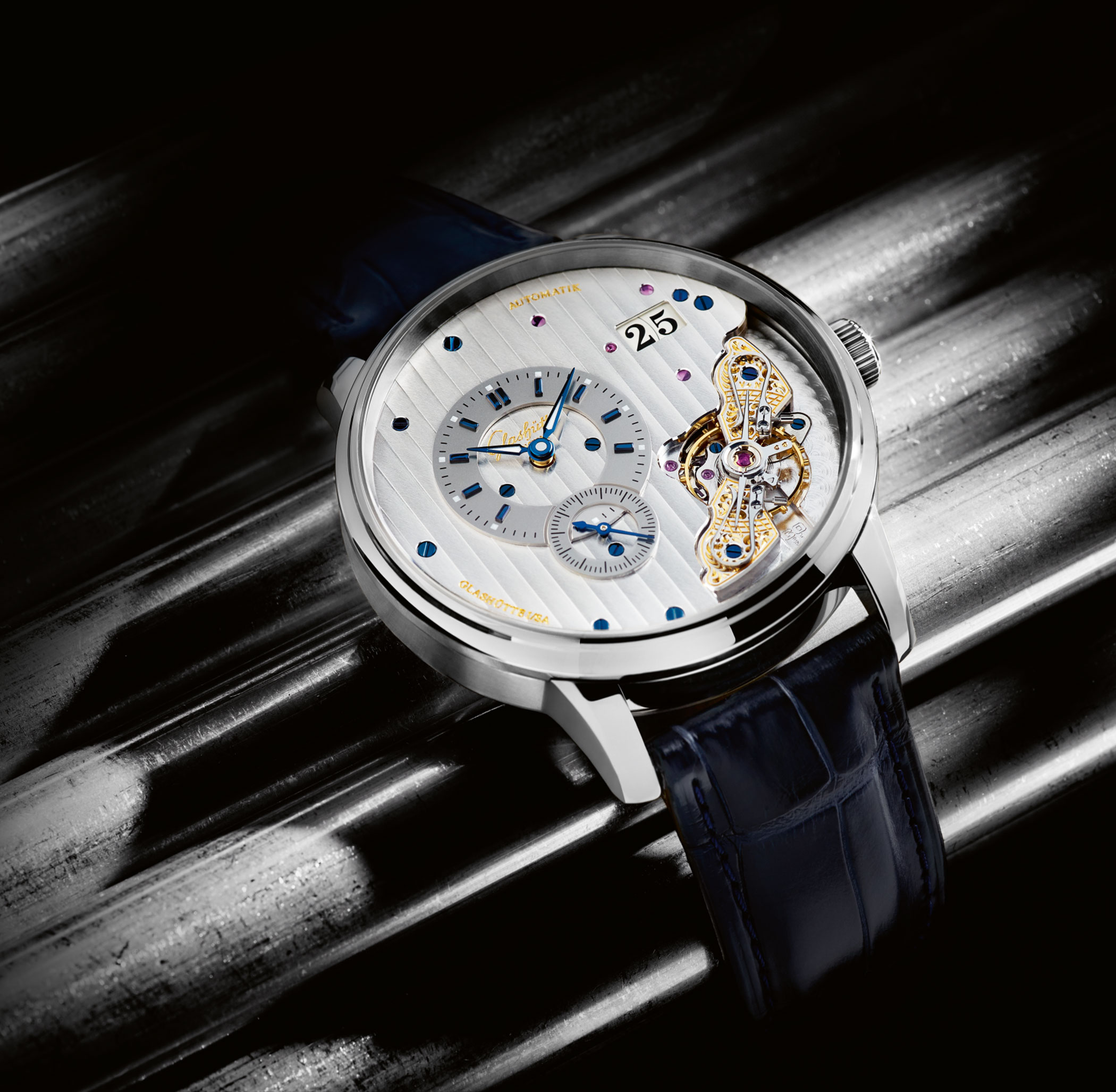 Eine Glashütte Pano Maticinverse mit skelettiertem Zifferblatt, sichtbarem Uhrwerk, silbernem Gehäuse und blauem Lederarmband, auf glänzendem Untergrund präsentiert.