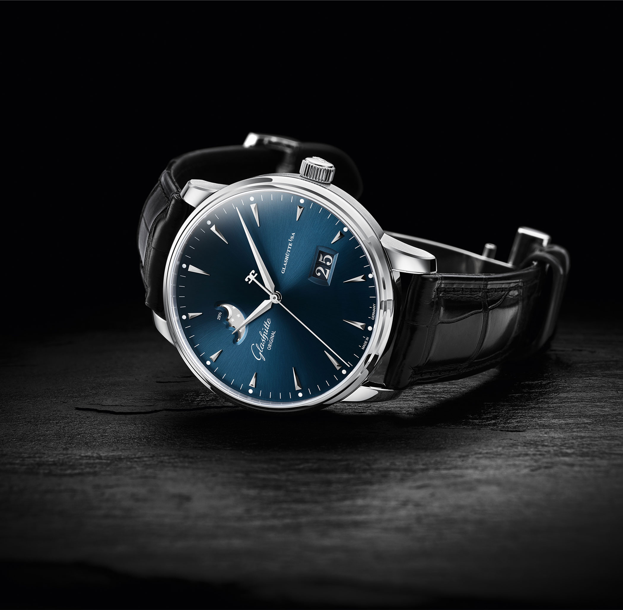 A Glashütte Original Senator with blue dial, moon phase display and panorama date, shown with black leather strap on a dark surface.