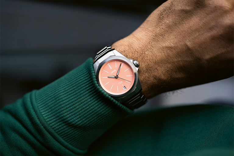Close-up of the Oris Propilot X Calibre 400 in a 39 mm titanium case with a salmon-colored dial on the wrist of a man wearing a dark green sweater.