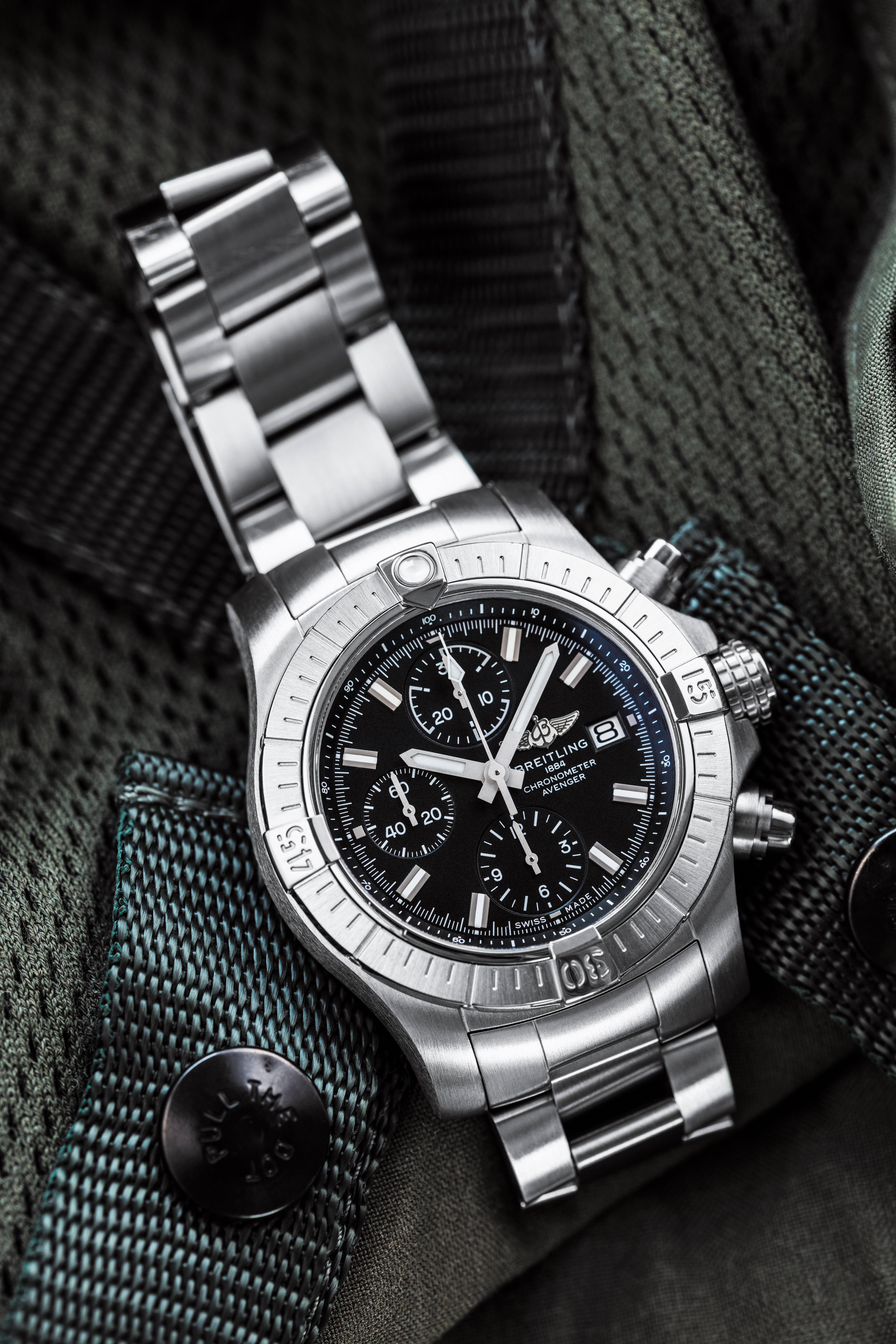 A Breitling “Avenger Chronograph 43” with steel bracelet and unidirectional rotating bezel on a black fabric background.