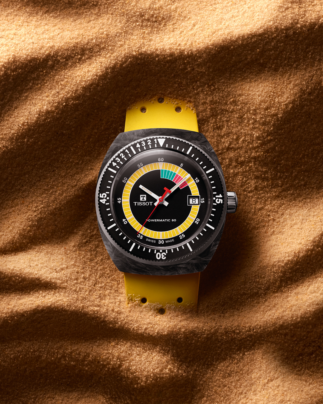 Tissot Sideral Powermatic 80 with black carbon case, colorful dial, and yellow rubber strap on a sandy background