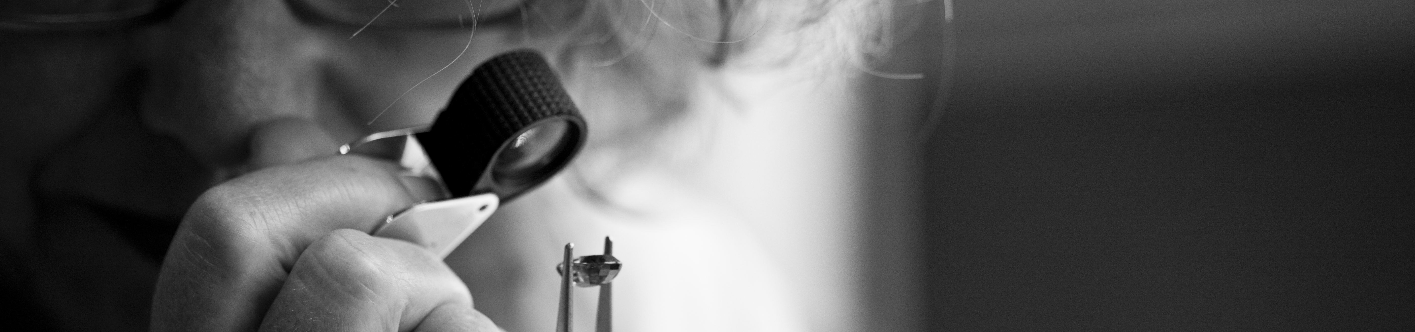 A jeweler in works on a small metal piece with precision tools in a well-lit workshop