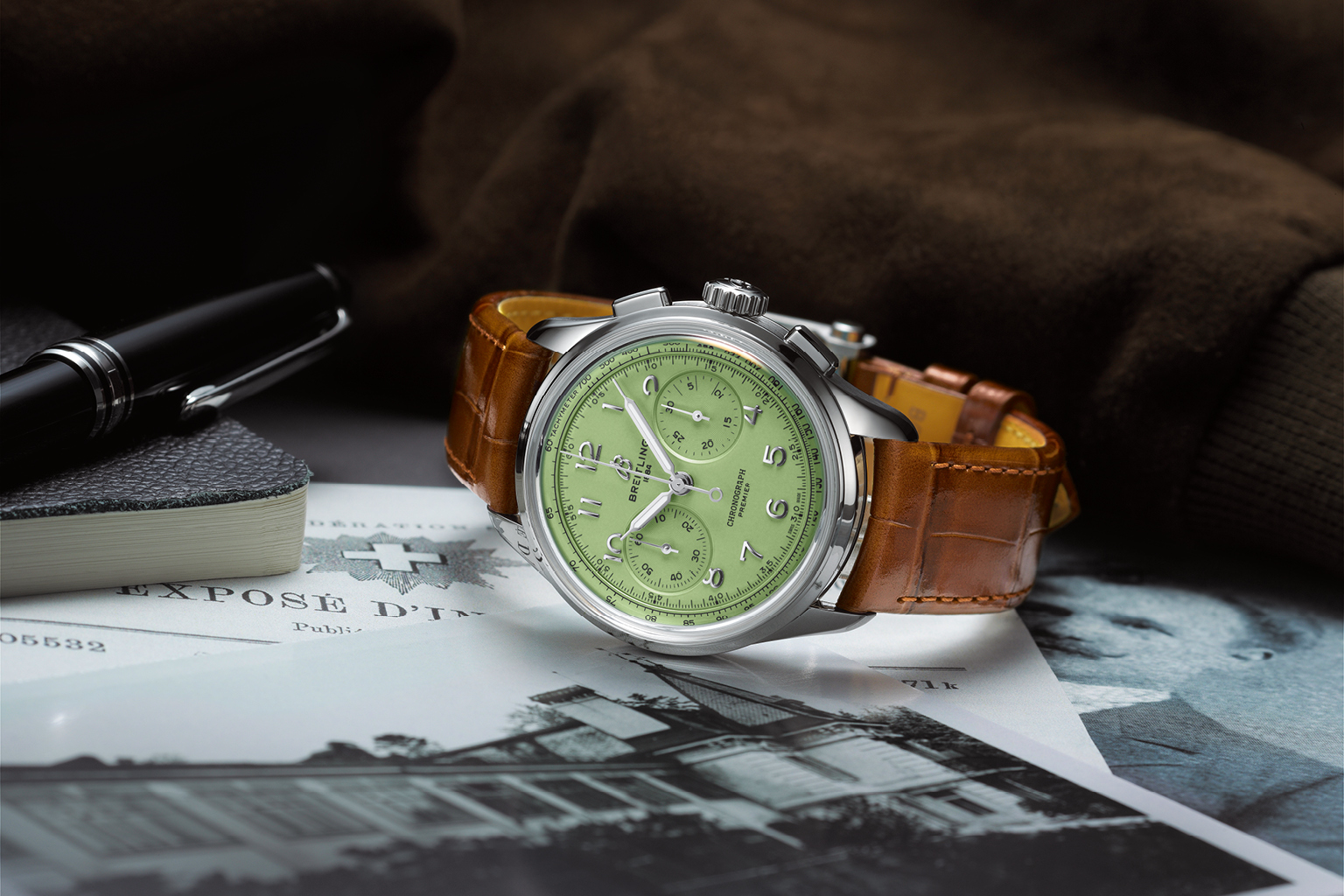 A Breitling “Premier B09 Chronograph 40” with a brown leather strap and green dial lies on brochures.