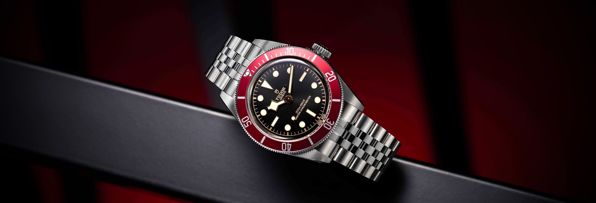 Banner featuring the Tudor dive watch with a black dial, bold luminous hour markers, and a stainless steel bezel, set against a dynamic background with metallic and red accents. The Tudor logo is displayed prominently on the right side, highlighting the brand’s elegance and robust design