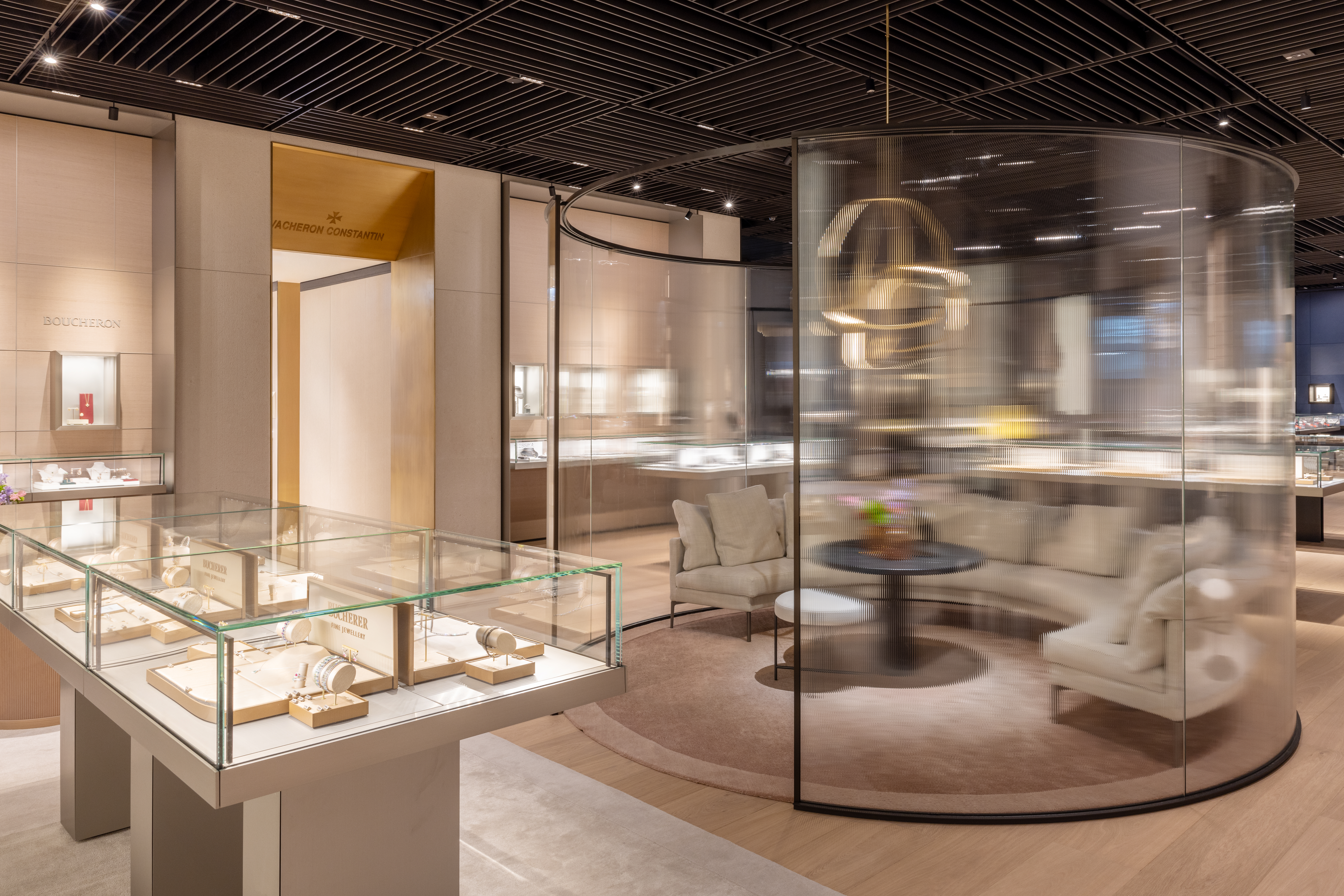 A luxury jewelry store interior with glass display cases, a curved glass partition, and a seating area.