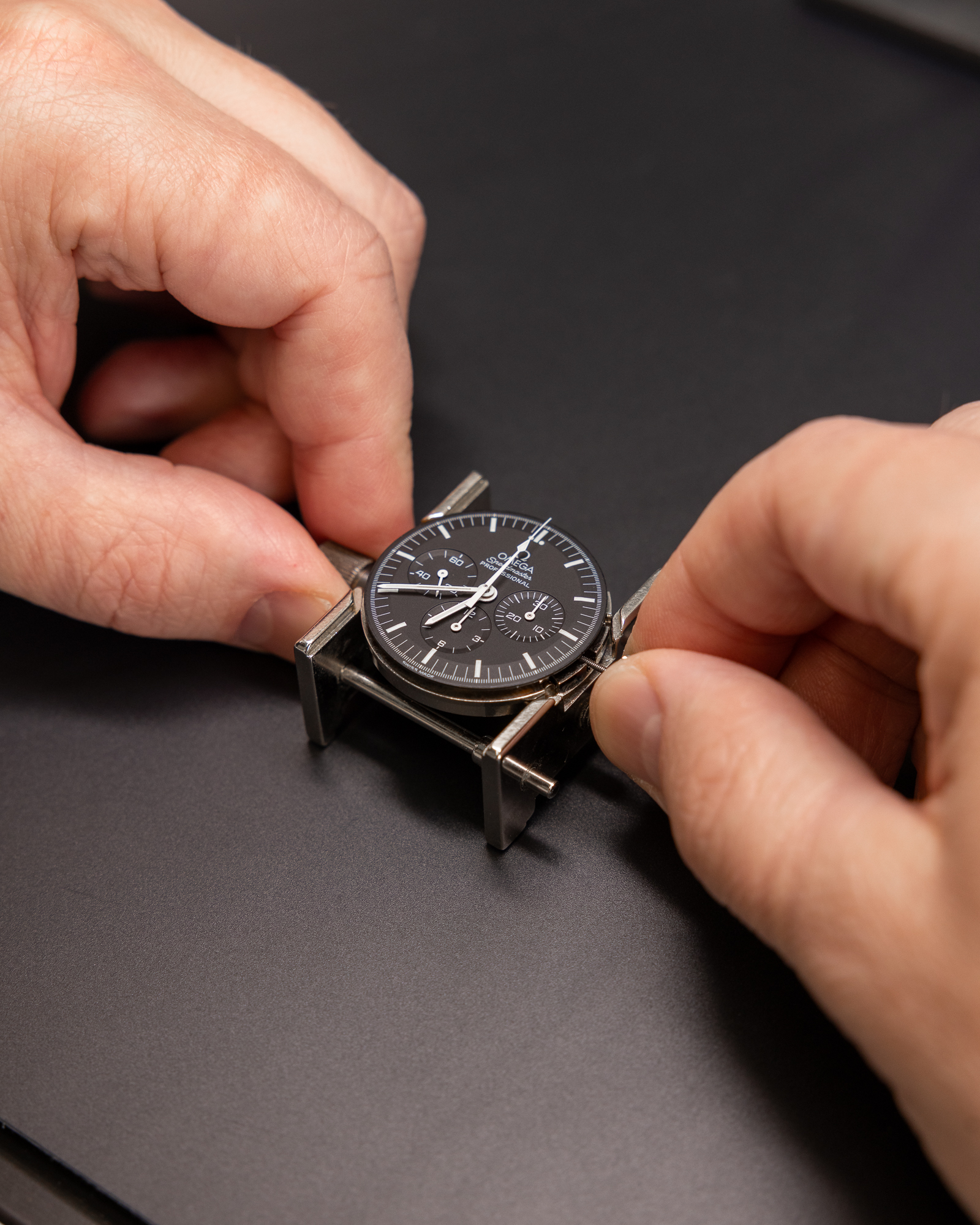 Hands adjusting a black chronograph watch with a metal bezel on a dark surface.
