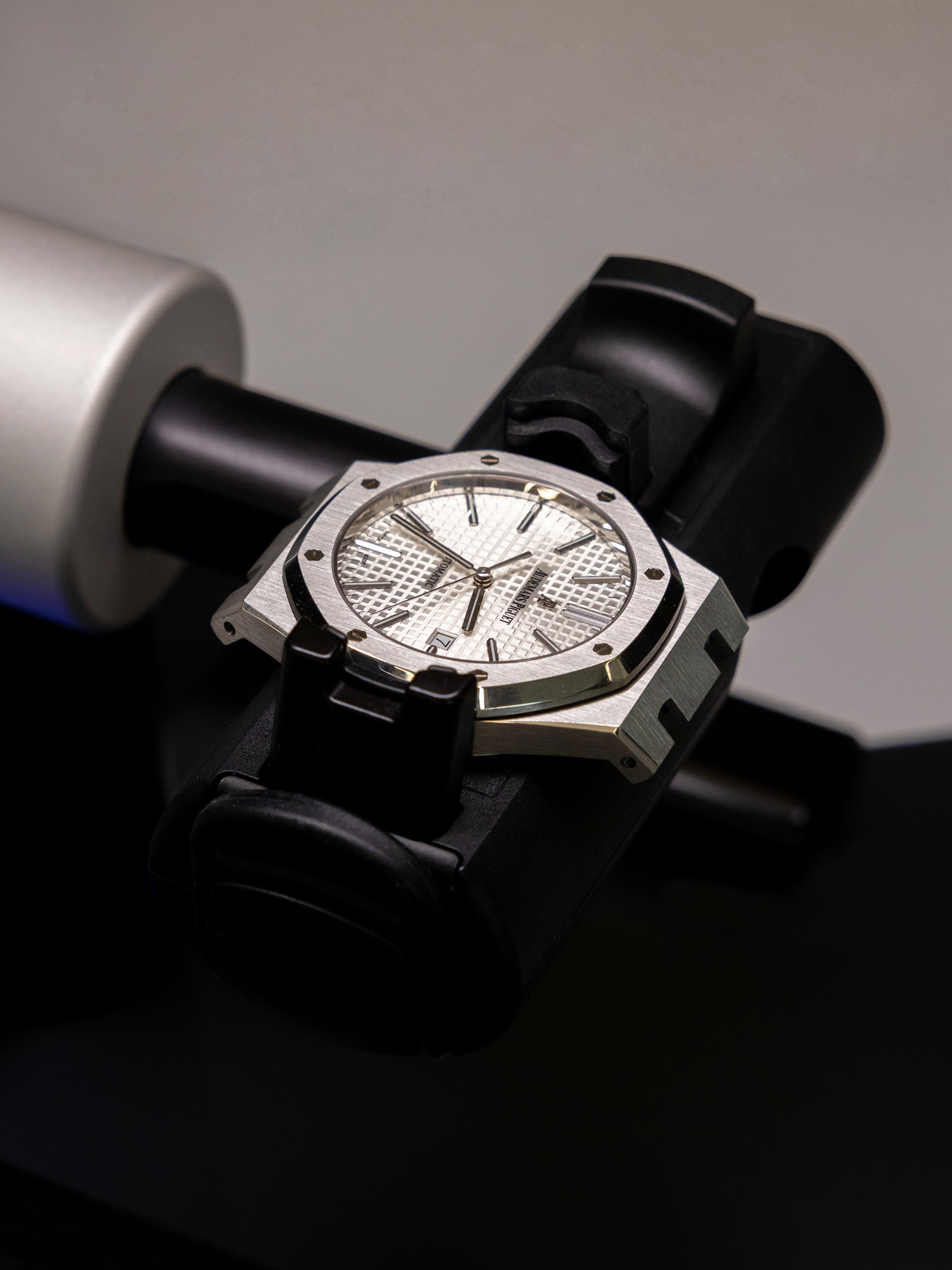 Silver Audemars Piguet Royal Oak watch with a white dial and black rubber strap, displayed on a black stand.
