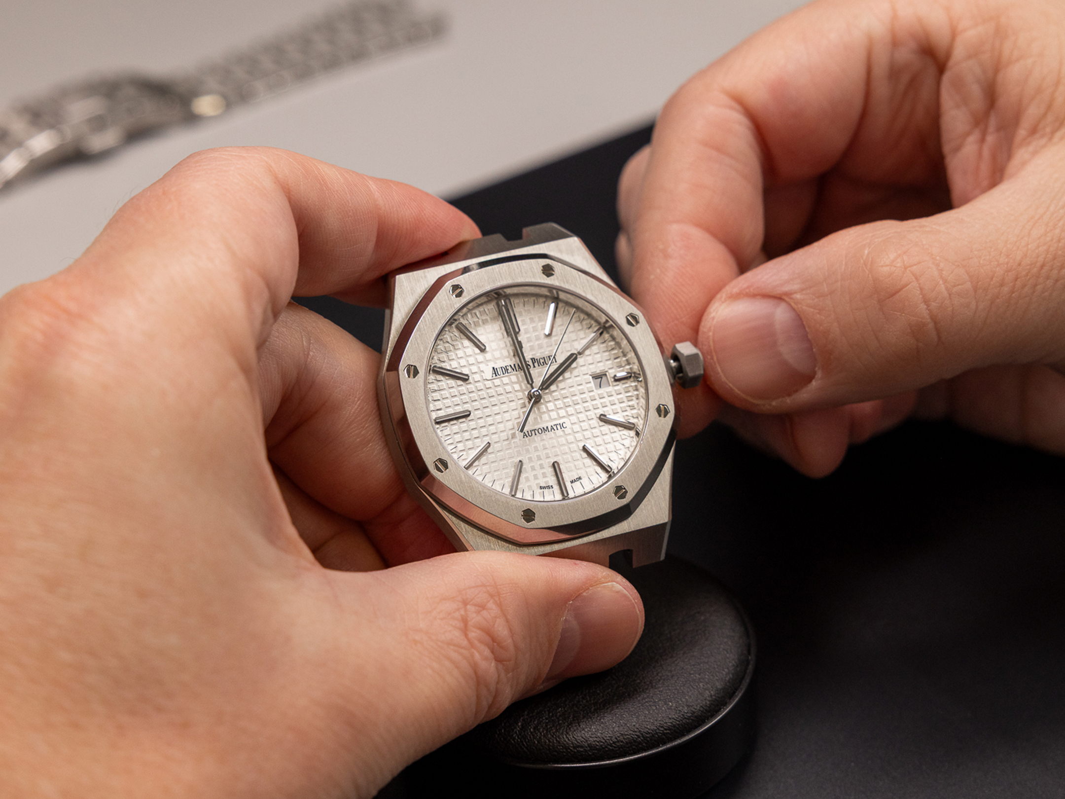 Hands hold a silver Audemars Piguet Royal Oak watch with a white dial and visible movement.