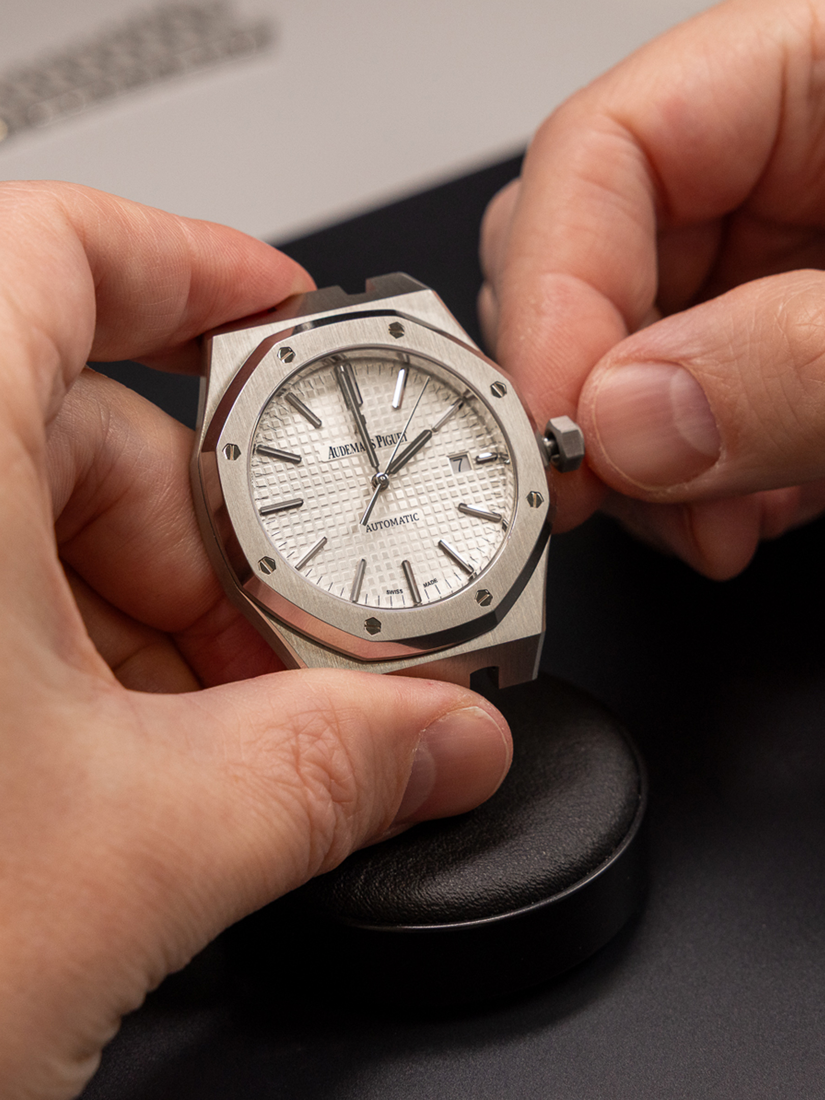 Hands adjusting the crown of a silver Audemars Piguet Royal Oak watch with a white dial.