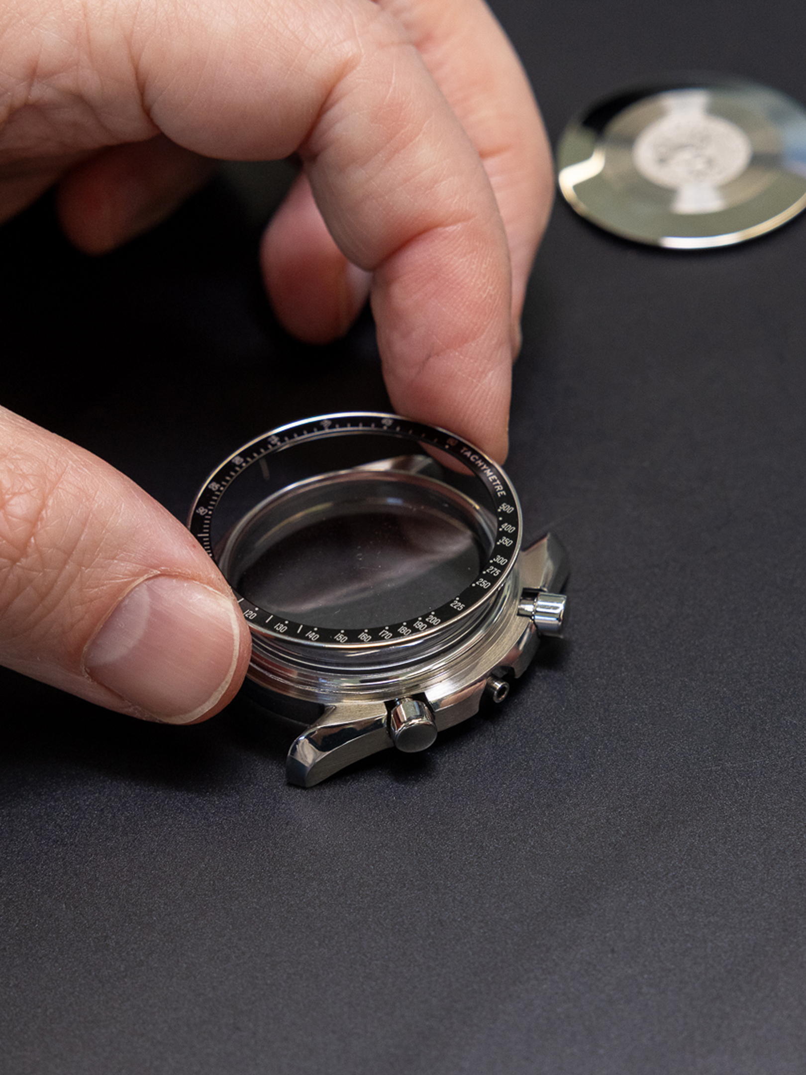 A person's hands assembling a watch, placing a clear crystal and bezel onto the watch case.