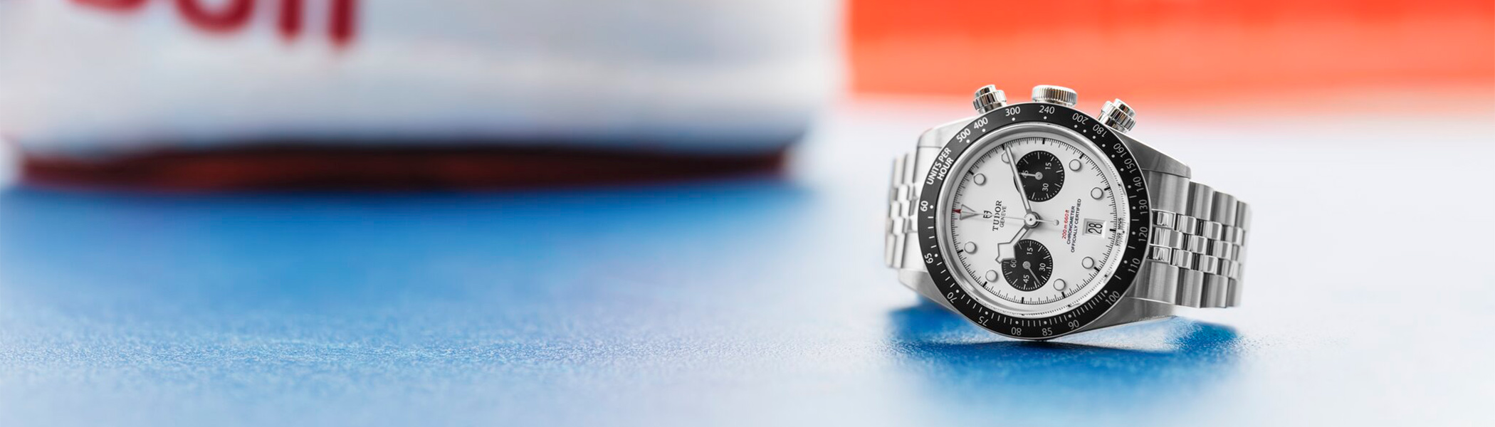 Banner featuring the Tudor dive watch with a black dial, bold luminous hour markers, and a stainless steel bezel, set against a dynamic background with metallic and red accents. The Tudor logo is displayed prominently on the right side, highlighting the brand’s elegance and robust design