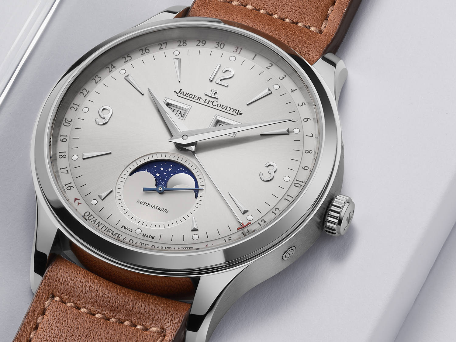 Close-up: silver-colored dial of a Jaeger-LeCoultre Master Control Calendar with leather strap on a white surface.