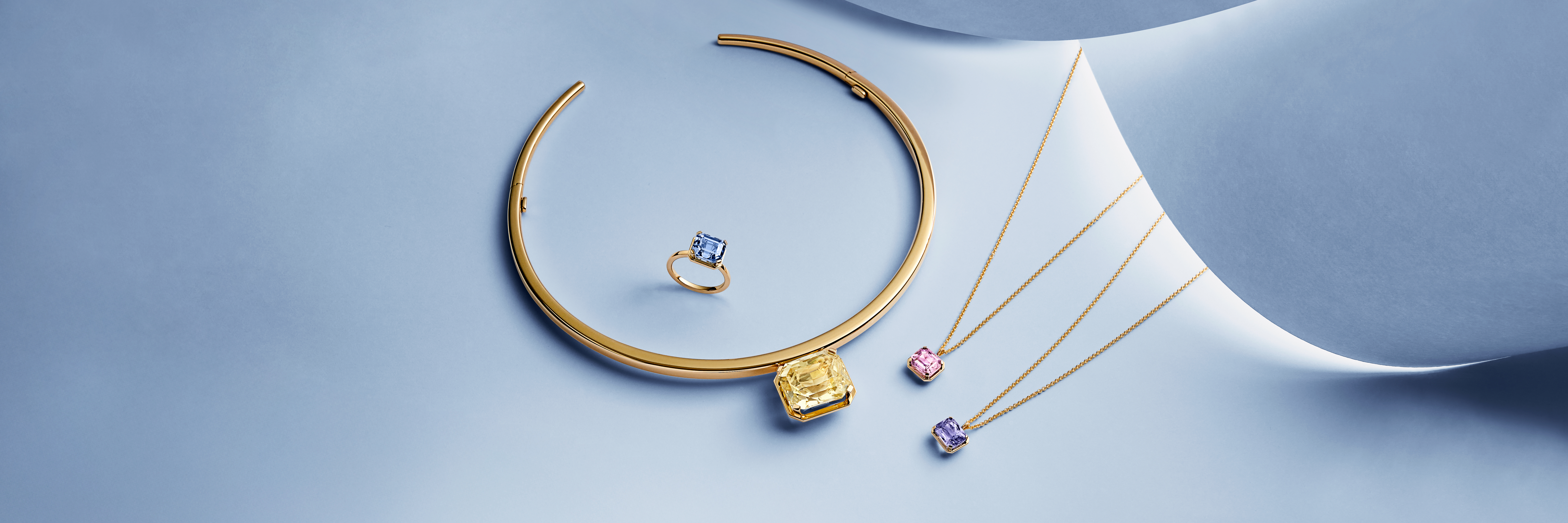 Emerald-cut indigo tourmaline ring set in yellow gold from the Bucherer Fine Jewellery Blue Path Collection, displayed against a soft blue background.