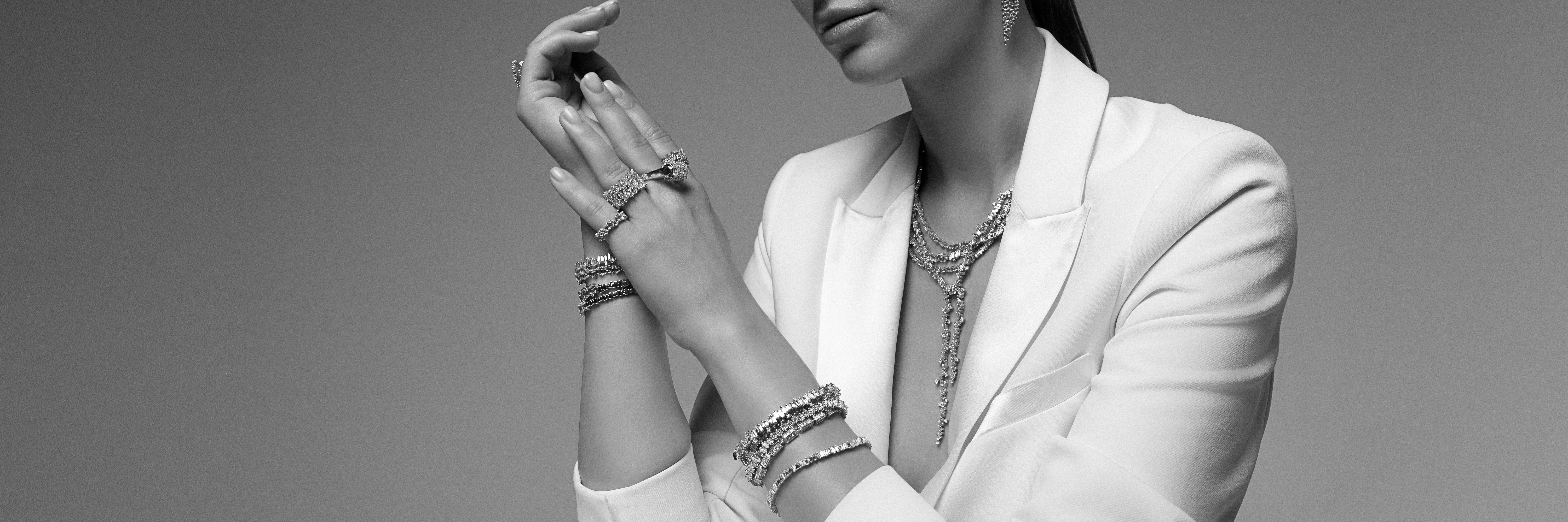 Model wearing a white suite and stacks of bracelets and necklaces.