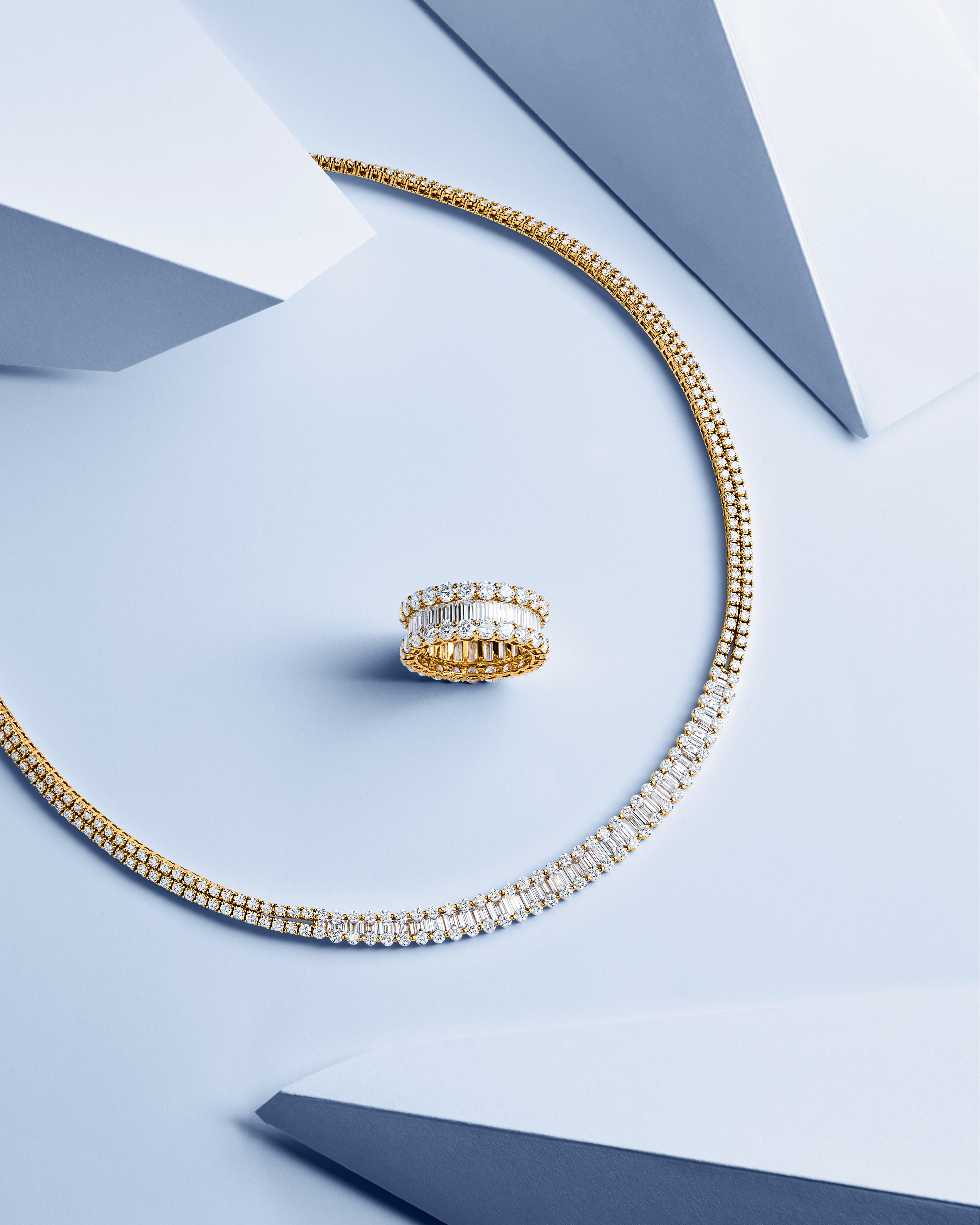 Bucherer Fine Jewellery earrings featuring a half-hoop design, adorned with sparkling baguette-cut diamonds and a surrounding row of round diamonds. The elegant earrings are displayed on a soft blue background, emphasizing their brilliance and refined craftsmanship.
