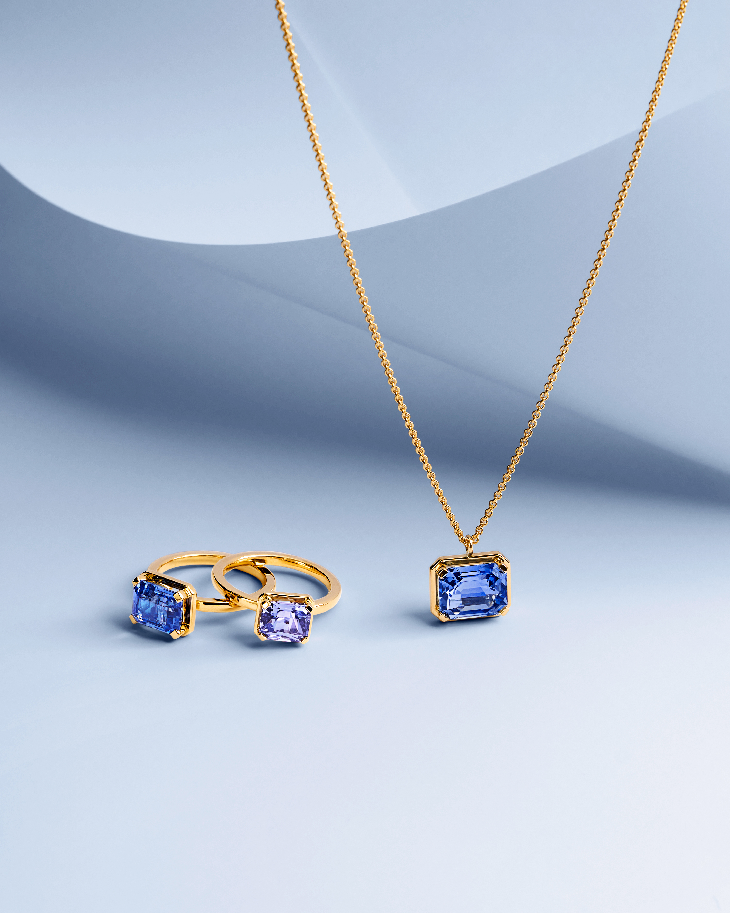 Gold necklace with a rectangular blue gemstone pendant and two gold rings with blue and purple rectangular gemstones.