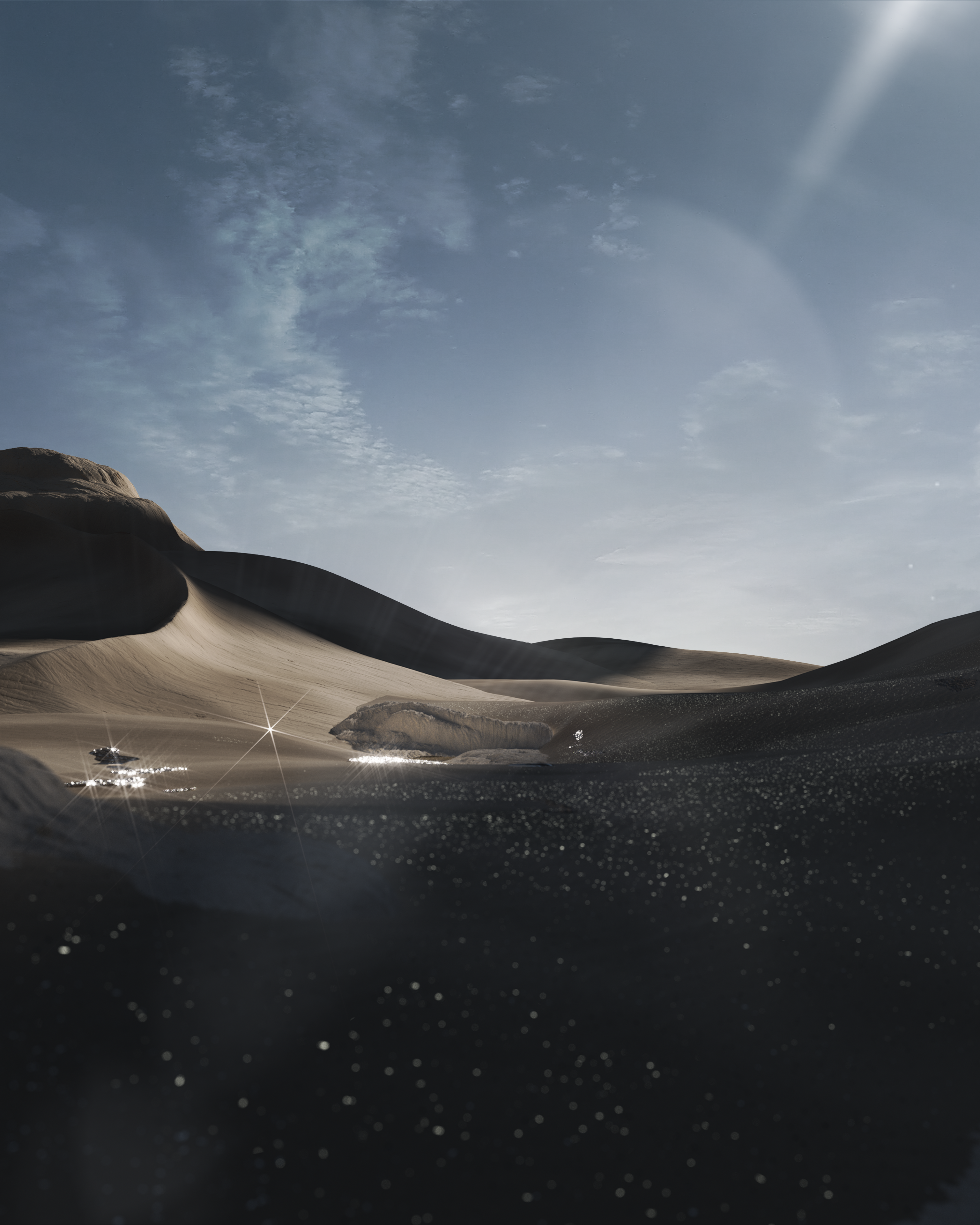 A desert landscape with dark sand in the foreground, light brown dunes in the background, and a small pool of water reflecting sunlight.