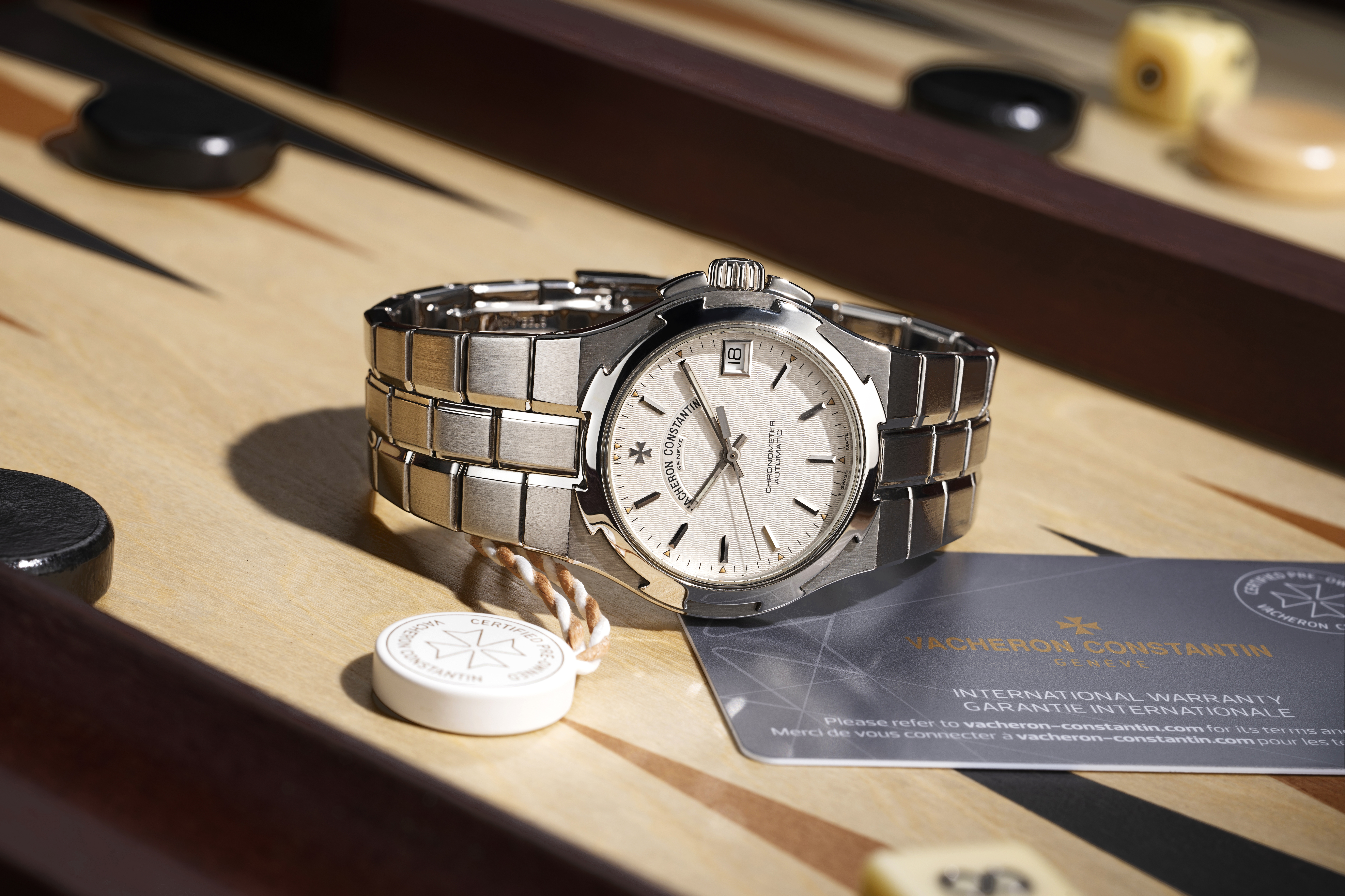 Eine silberne Vacheron Constantin Uhr mit weißem Zifferblatt und Garantiekarte auf einem Backgammon-Brett.