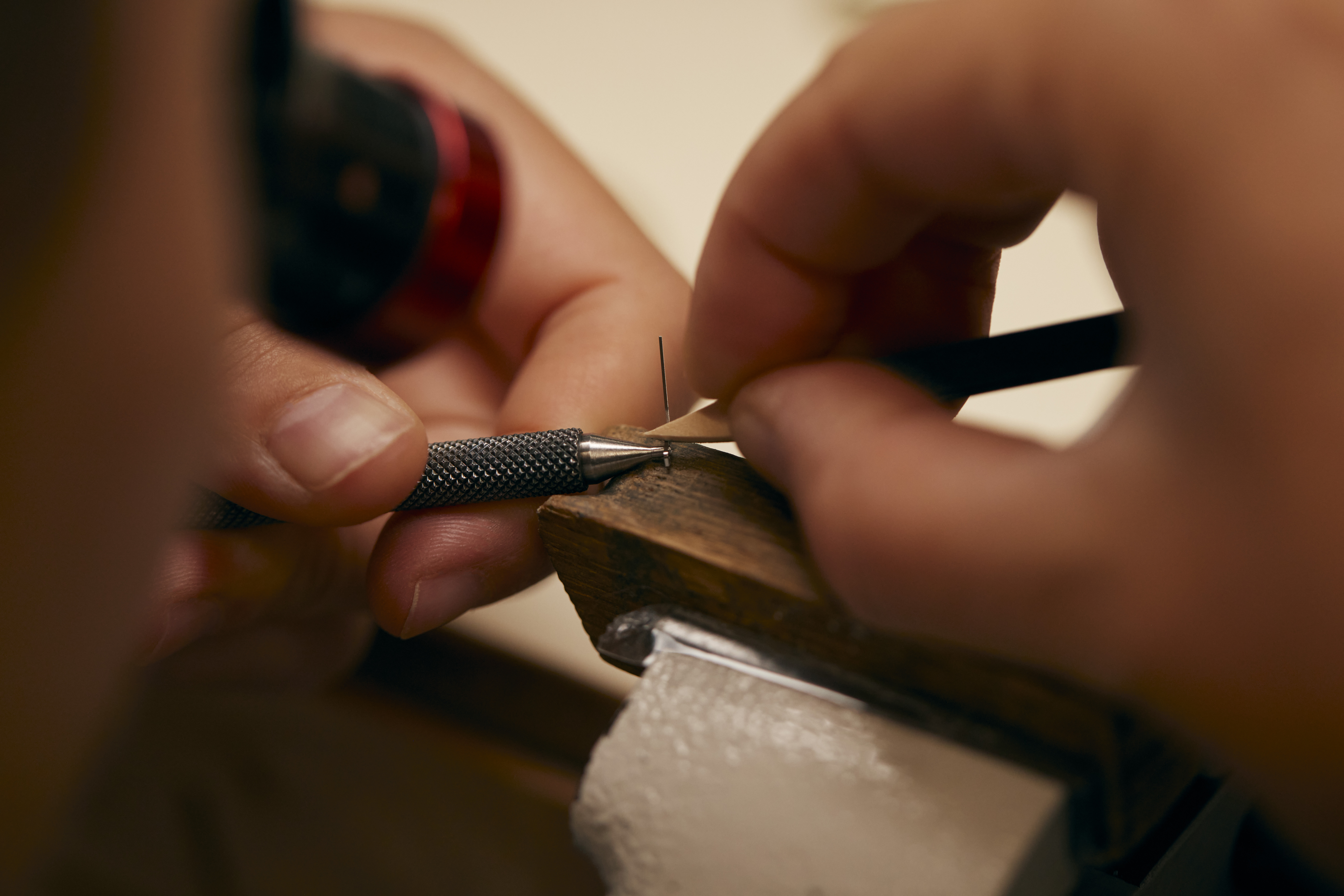Hands using a precision tool to work on a small object held in a vise.