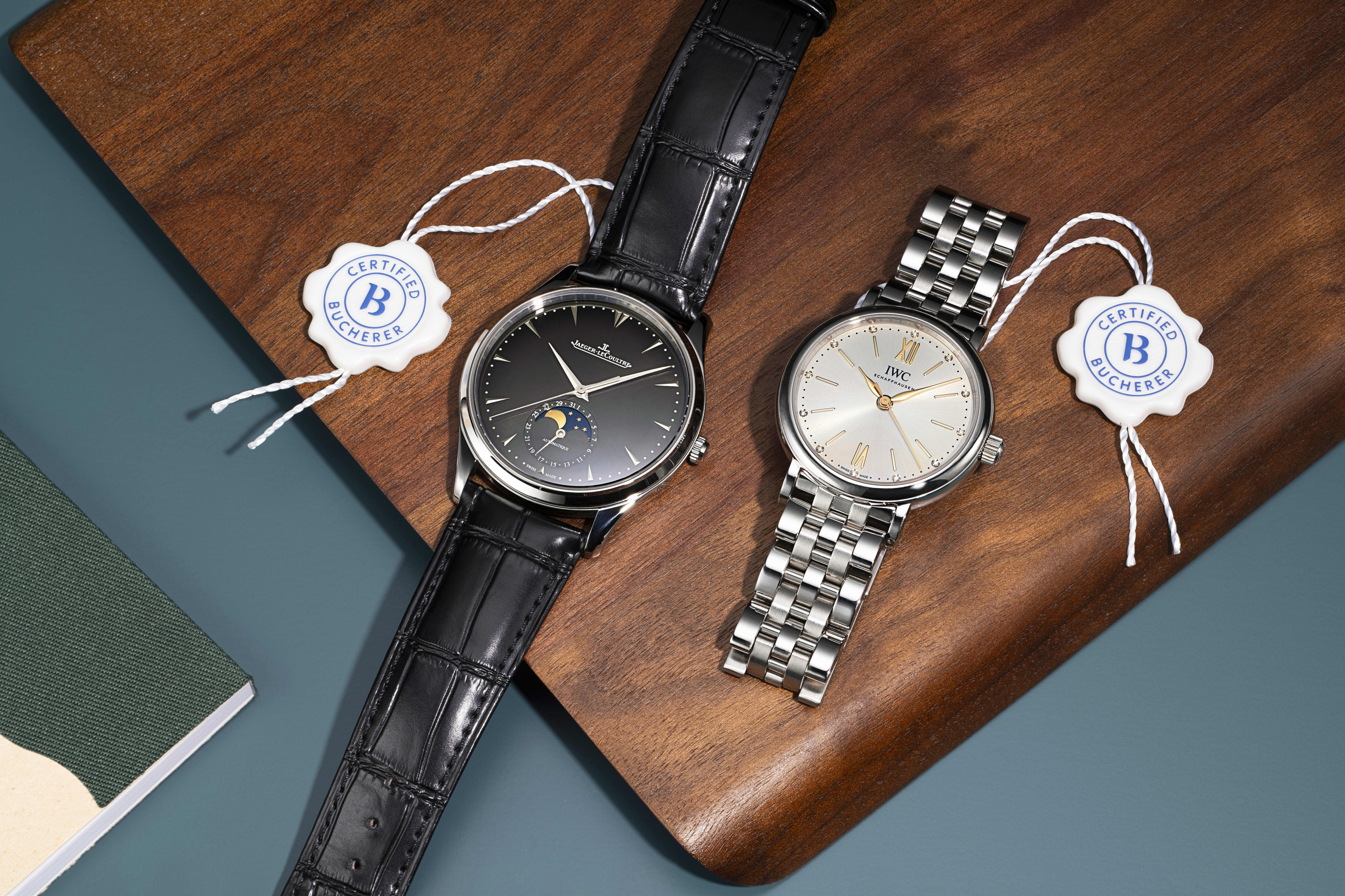 Two luxury watches, one with a black leather strap and the other with a silver metal bracelet, on a wooden surface.