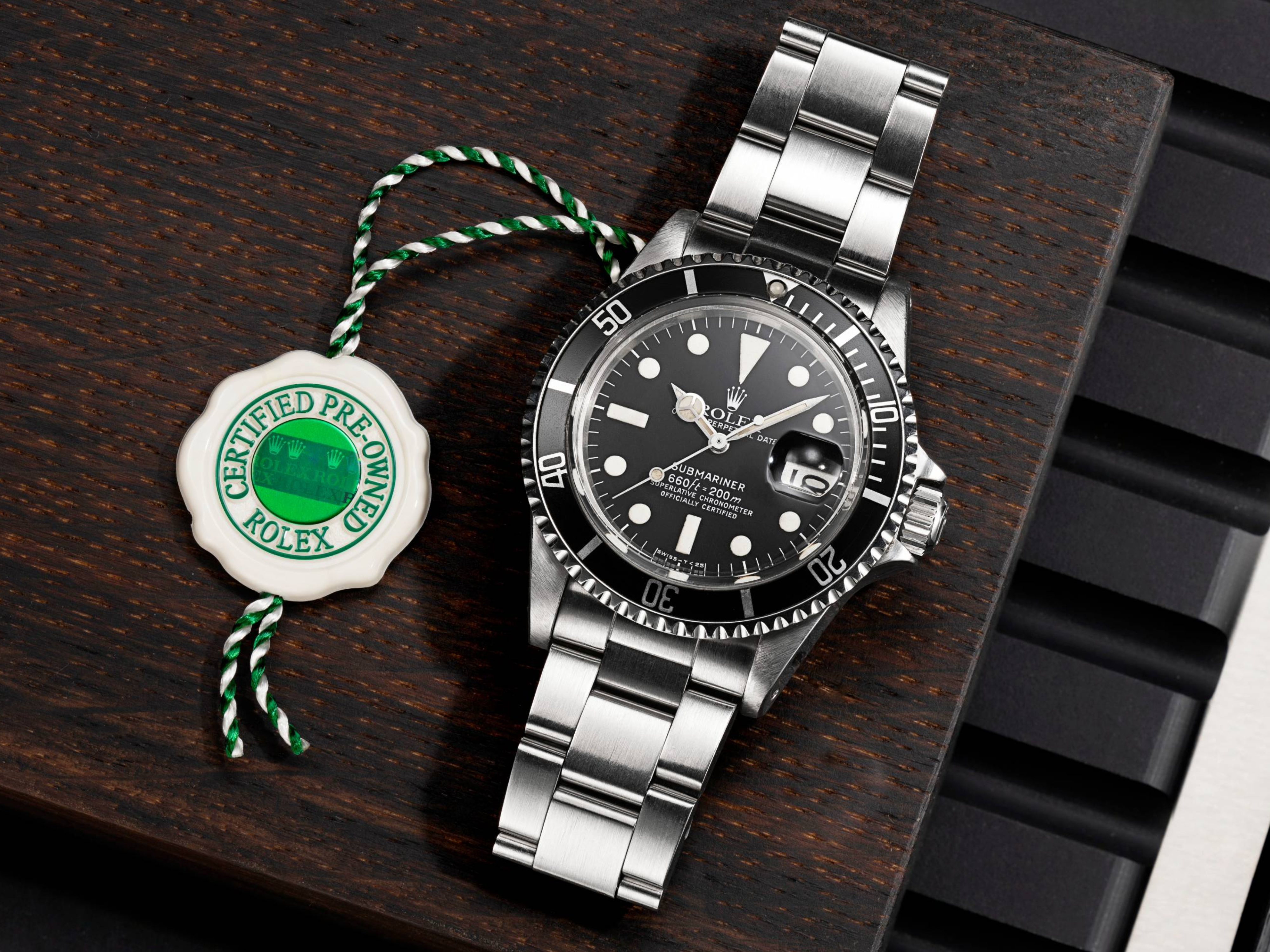 Une montre Rolex Submariner avec cadran noir et bracelet argenté, à côté d'une étiquette blanche et verte « Certifiée d'occasion ».