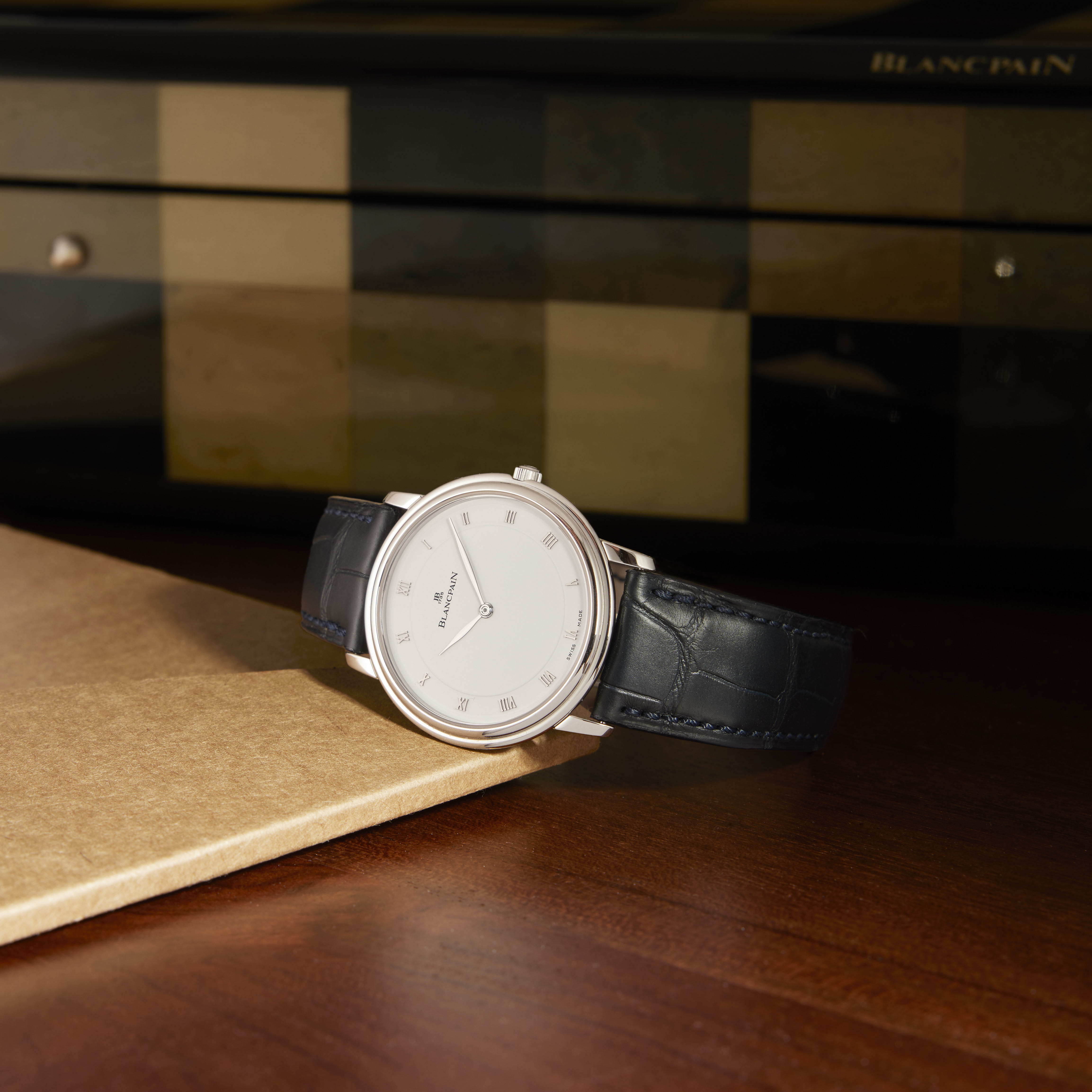 A silver Blancpain watch with a white face and dark blue leather strap rests on a wooden surface.