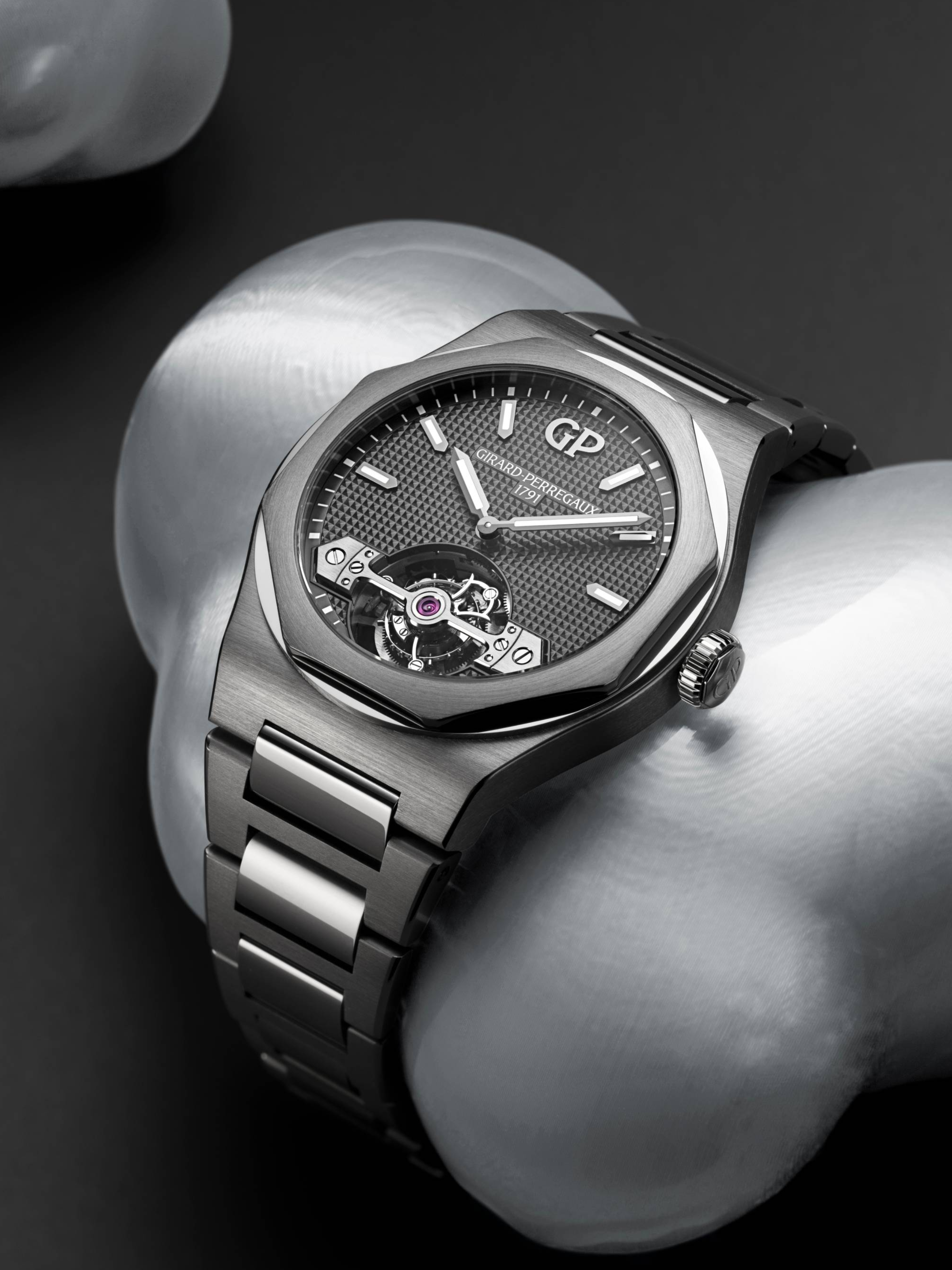 A silver Girard-Perregaux Laureato watch with a textured gray dial and visible tourbillon movement, resting on a metallic silver surface.