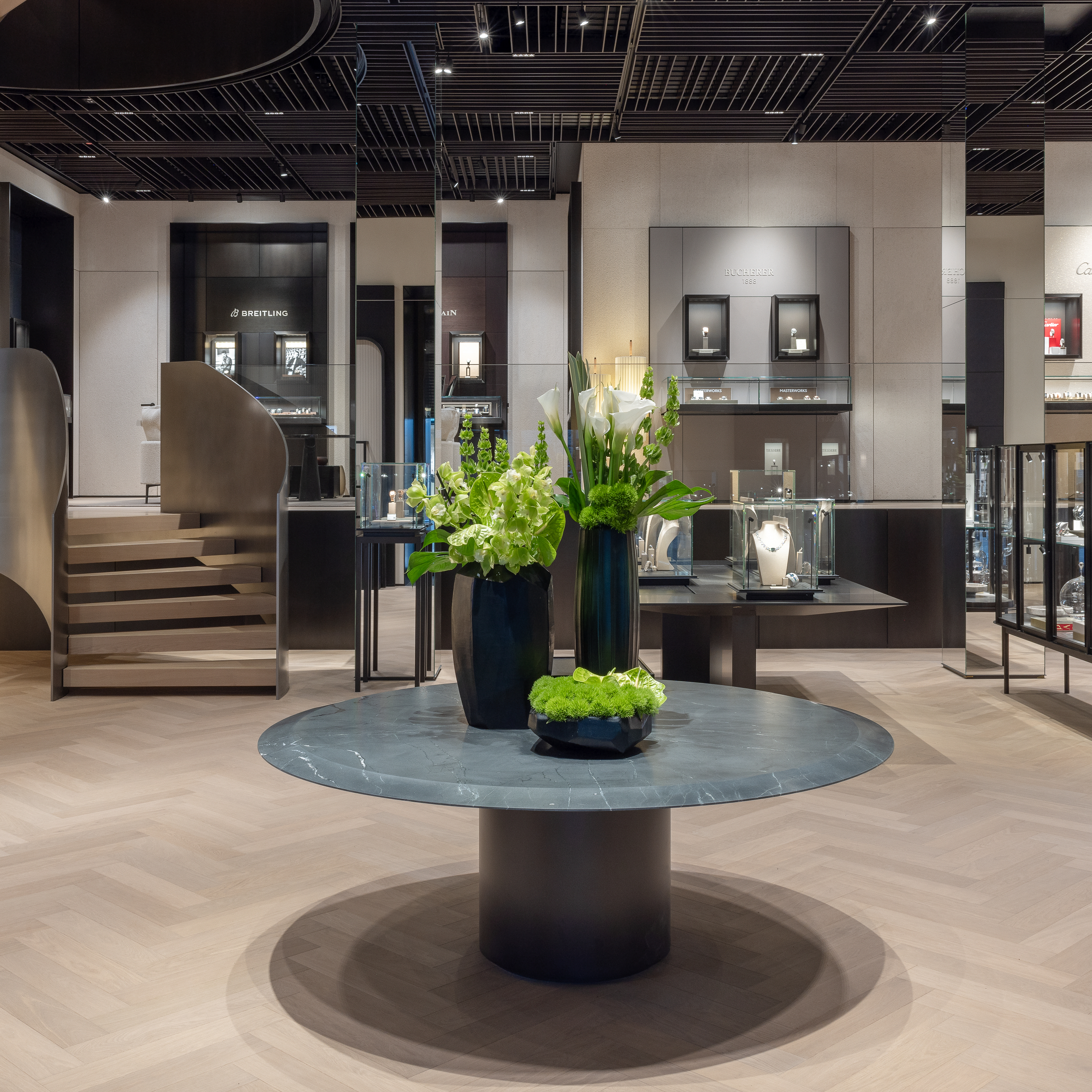 Das Interieur eines luxuriösen Uhren- und Schmuckgeschäfts mit einem runden Tisch, Blumenarrangements und Vitrinen.