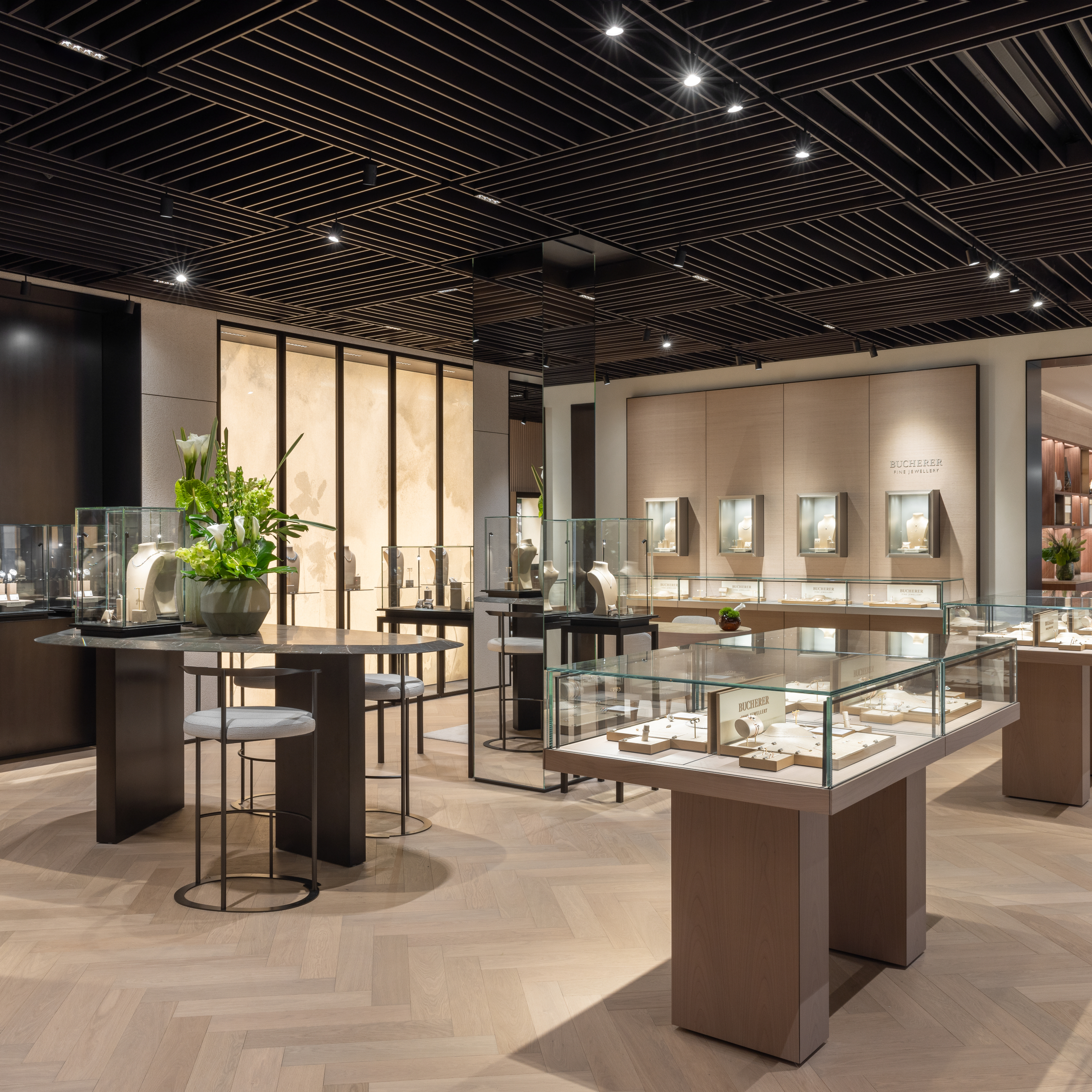 Das Interieur eines modernen Juweliergeschäfts mit Glasvitrinen, hellen Holzböden und einer dunklen Lamellendecke.