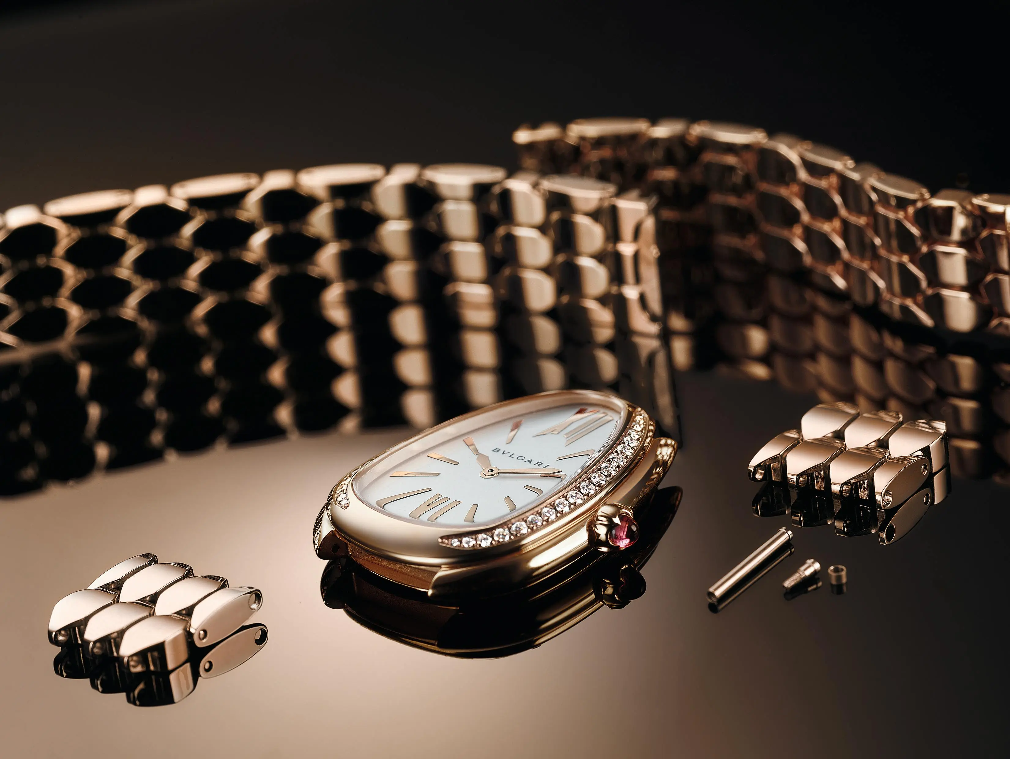 Eine goldene Bulgari Serpenti Uhr mit diamantbesetzter Lünette und weißem Zifferblatt, umgeben von zerlegten Goldgliedern.