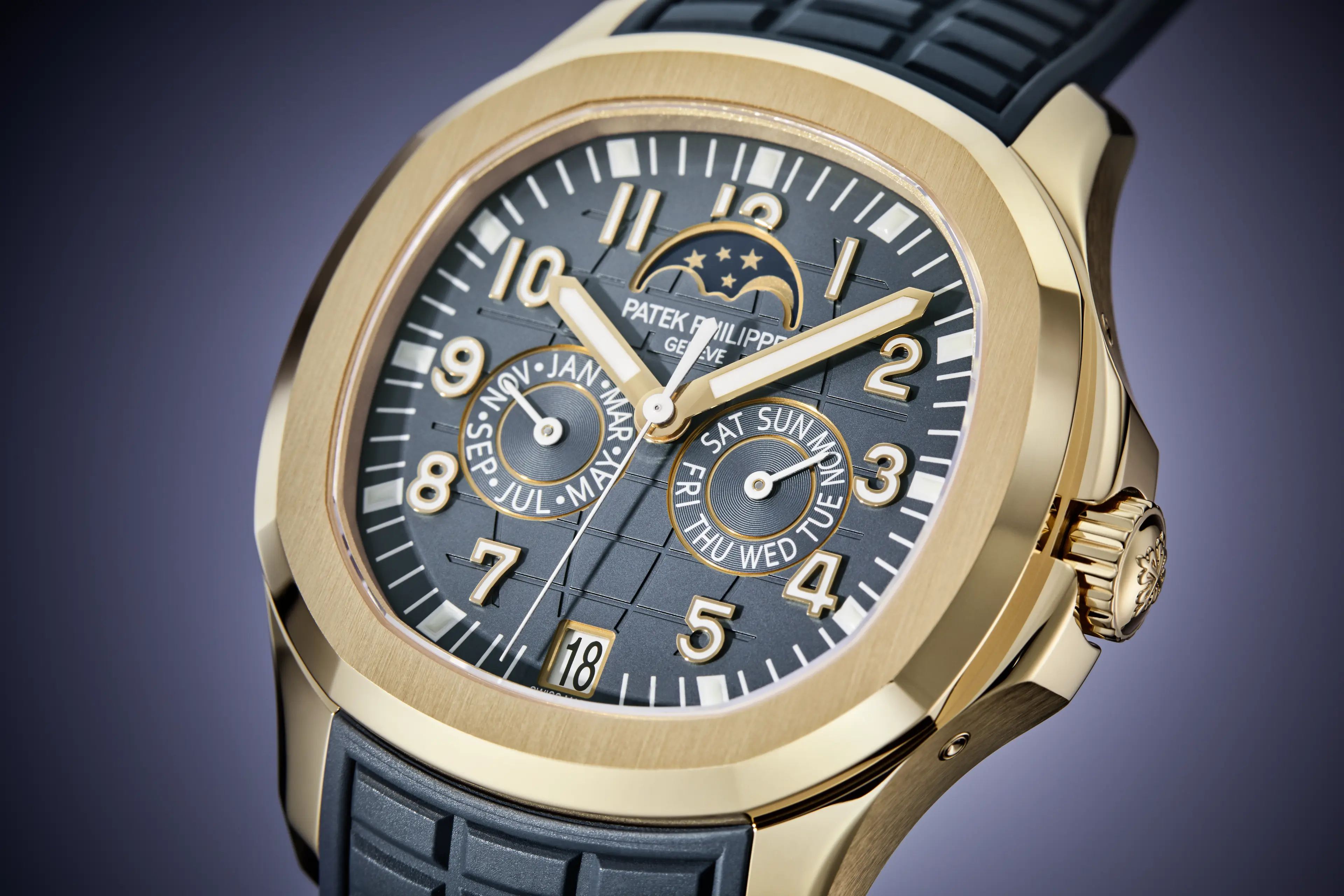 Gold Patek Philippe watch with a dark gray dial, gold numerals, and a dark gray rubber strap.