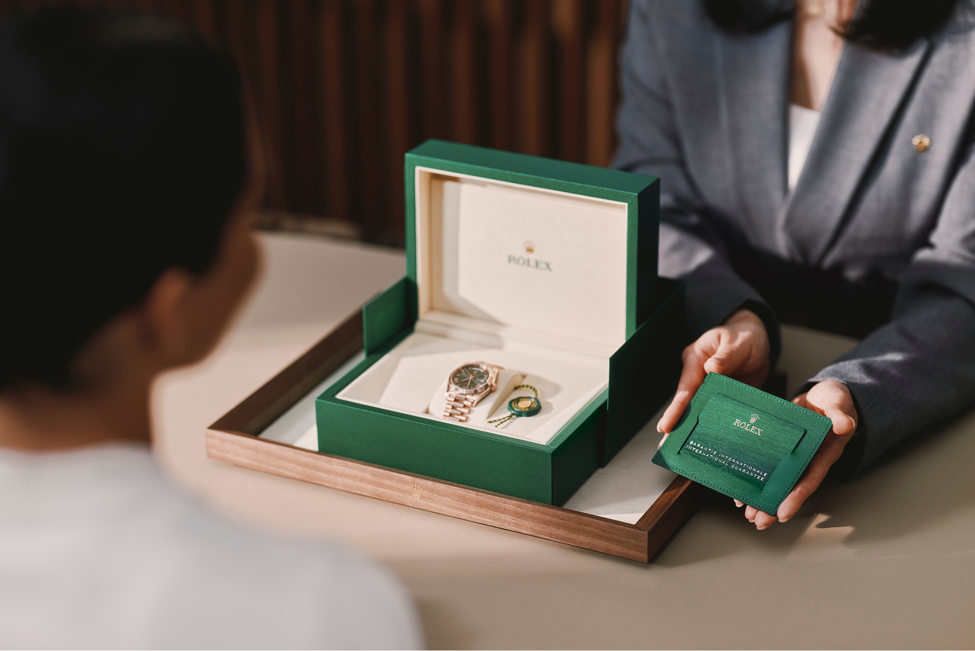 A Rolex watch in an open green box with a green leather card holder being presented to a customer.