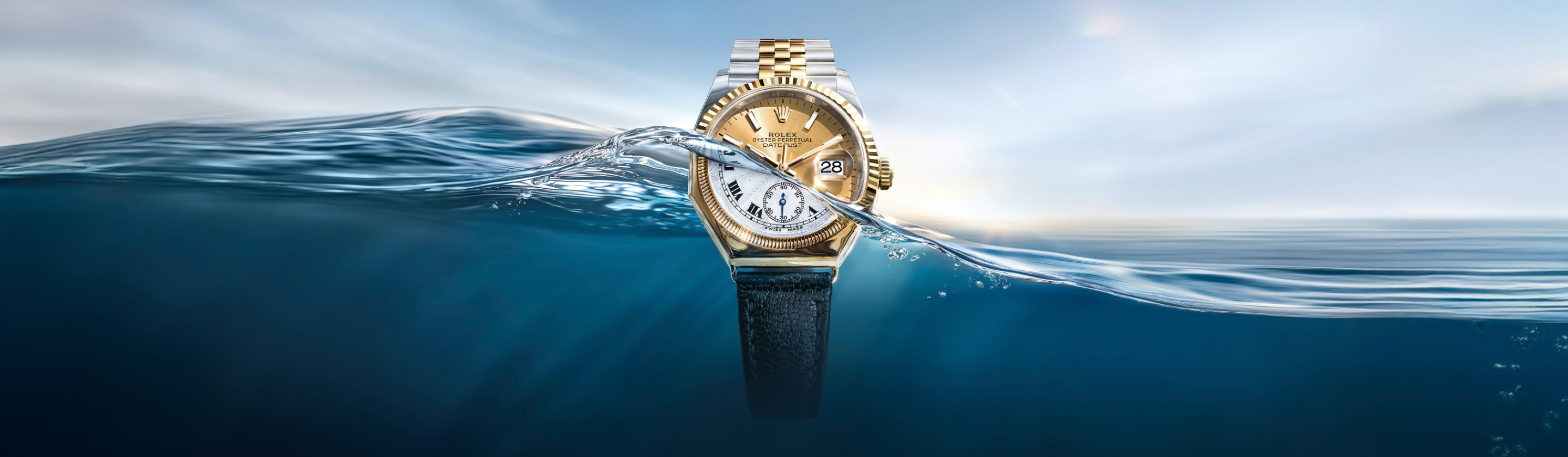 Eine goldene und silberne Rolex-Uhr mit schwarzem Lederarmband taucht aus blauem Wasser auf.
