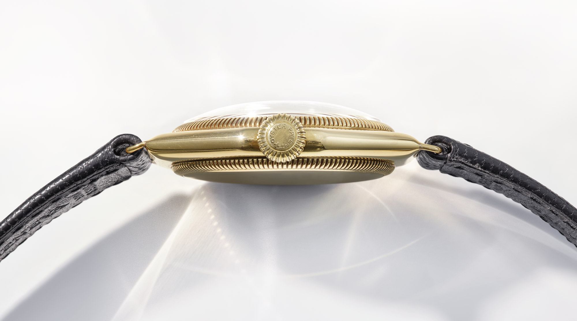 Seitenansicht einer goldenen Uhr mit geriffelter Lünette, Krone und schwarzem Lederarmband.