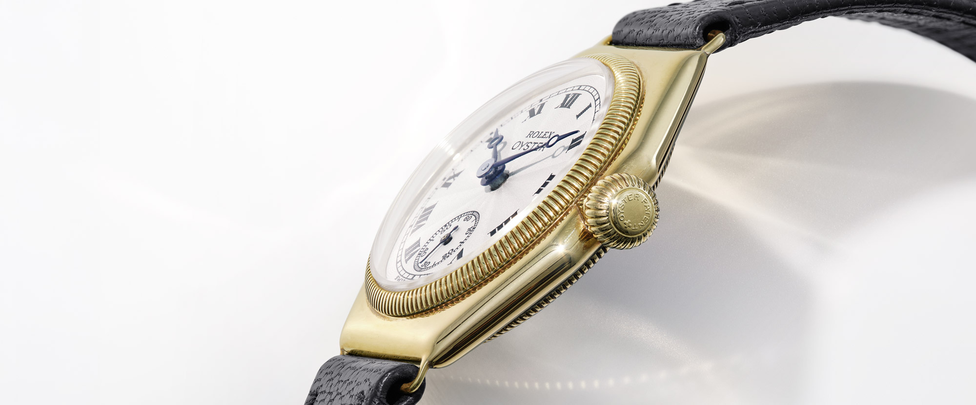 Eine goldene Rolex Oyster Uhr mit weißem Zifferblatt, römischen Ziffern und schwarzem Lederarmband.