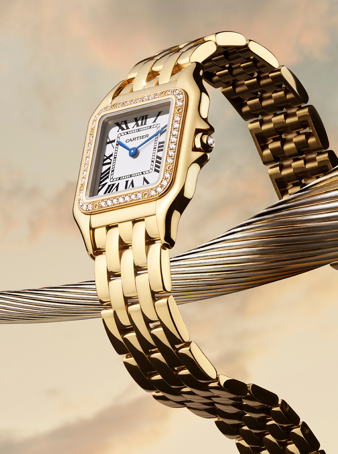 A gold Cartier Panthère watch with a diamond-encrusted bezel and white face with Roman numerals, draped over a metallic coil.