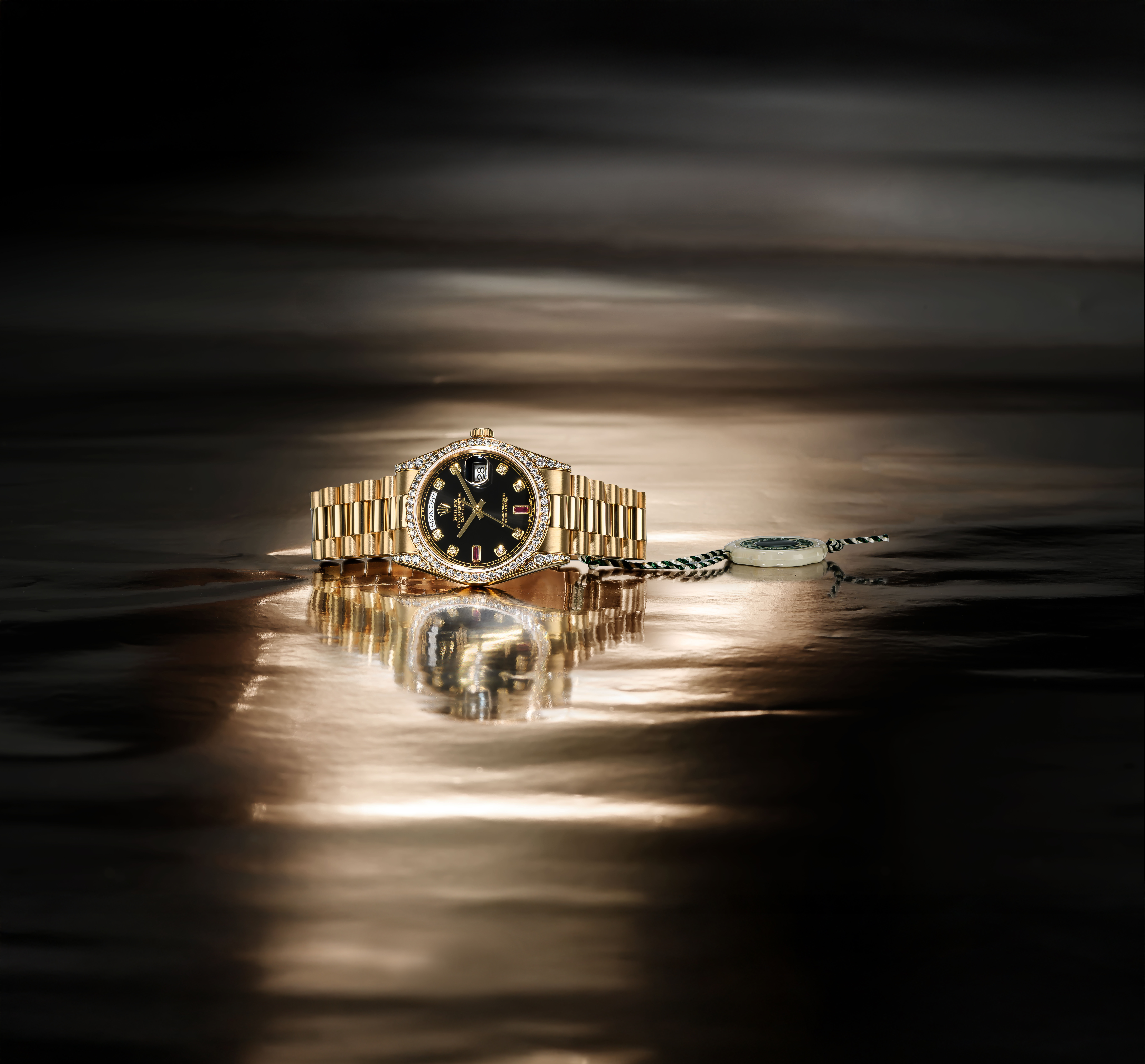 A gold Rolex watch with a diamond-encrusted bezel and black face, reflected on a shiny surface.