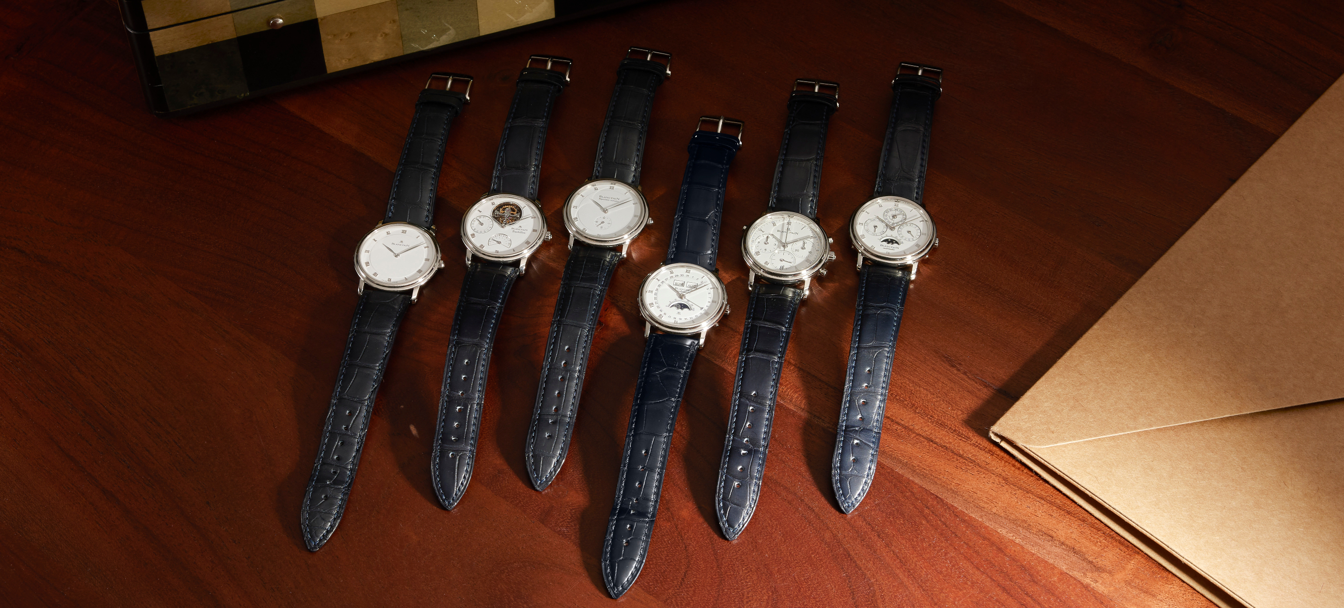 Six luxury wristwatches with white faces and dark leather bands arranged on a wooden surface.