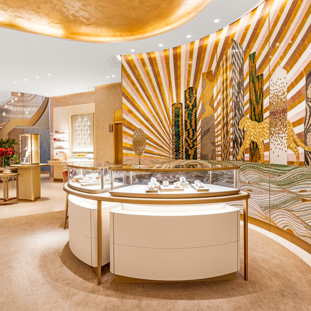 A luxury jewelry store interior with a curved display case in the foreground and a large, ornate mosaic wall art behind it.