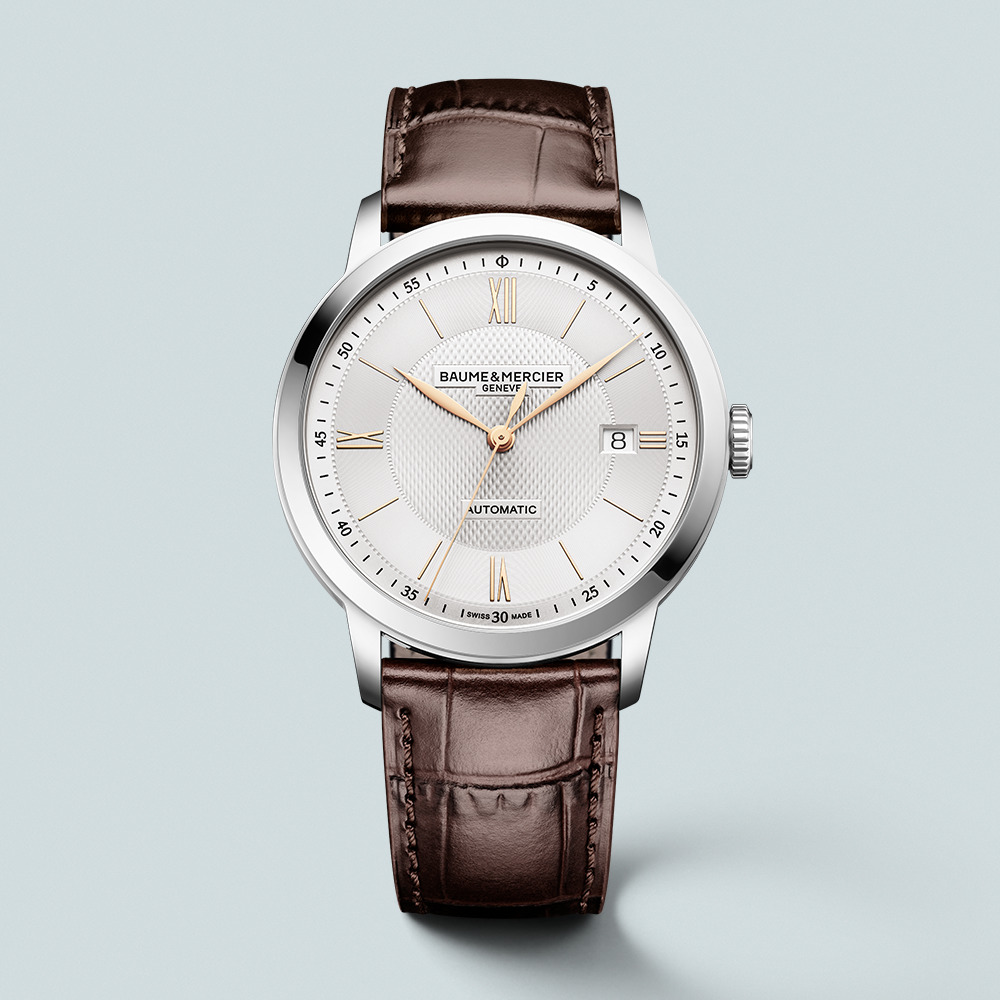 A silver Baume & Mercier automatic watch with a white face, gold hands, and a brown leather strap.