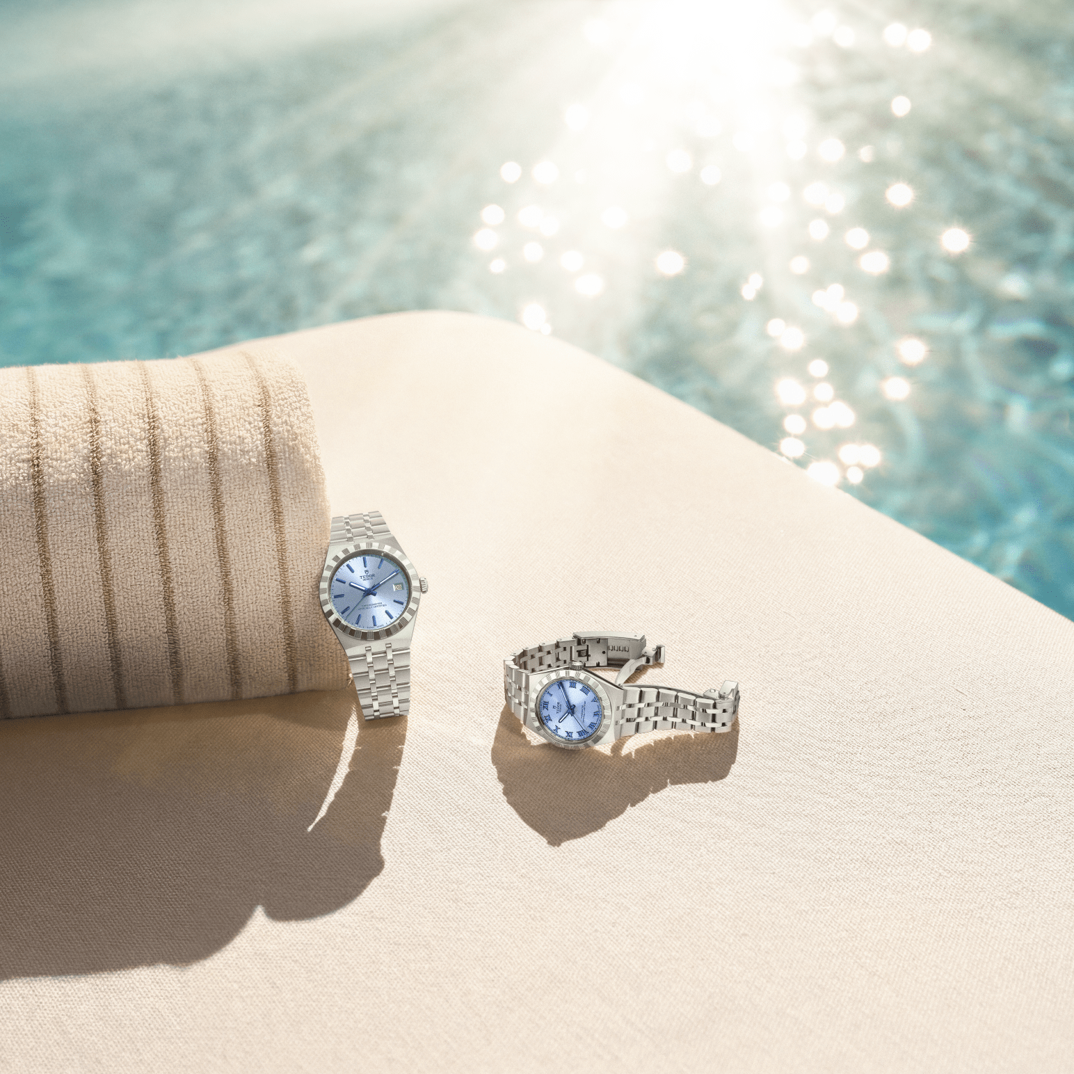 Two silver watches with light blue faces on a beige lounge chair next to a pool.