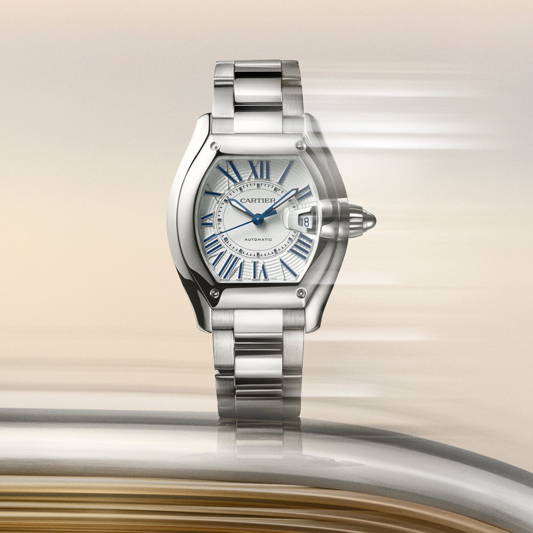 Silver Cartier watch with blue Roman numerals and hands, on a blurred background with horizontal streaks.