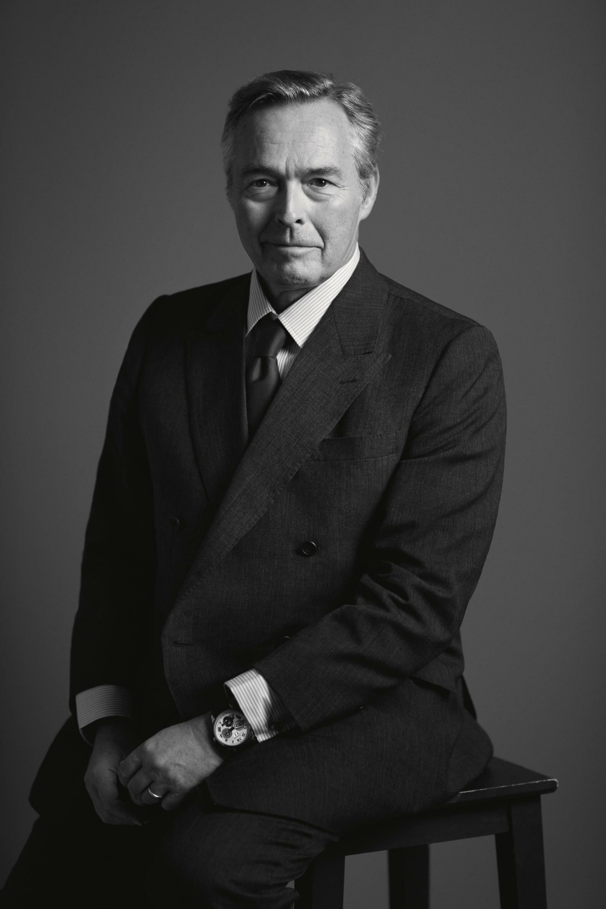 A middle-aged man in a suit and tie, with graying hair, looks directly at the viewer.