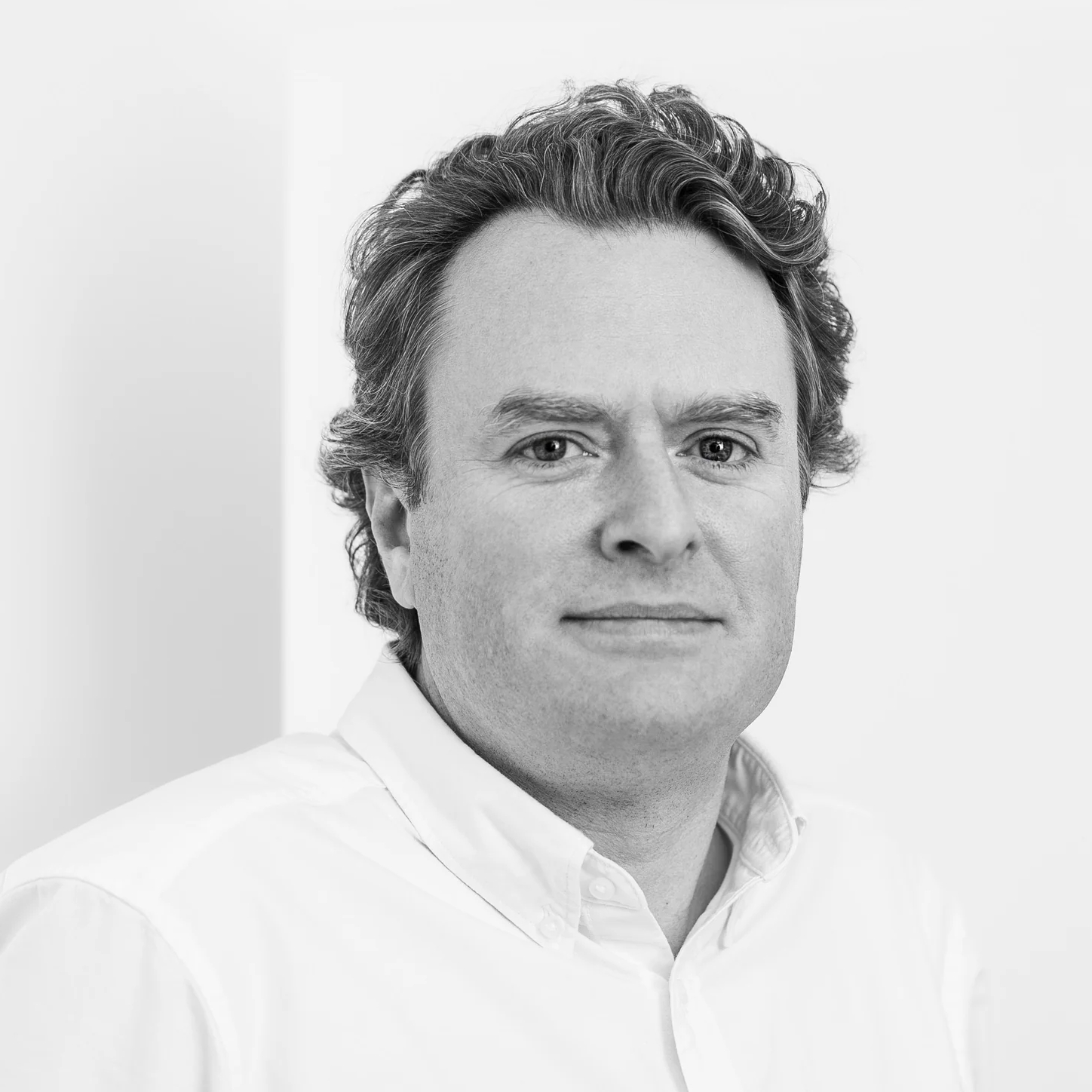 Black and white headshot of a man with curly hair wearing a white collared shirt.