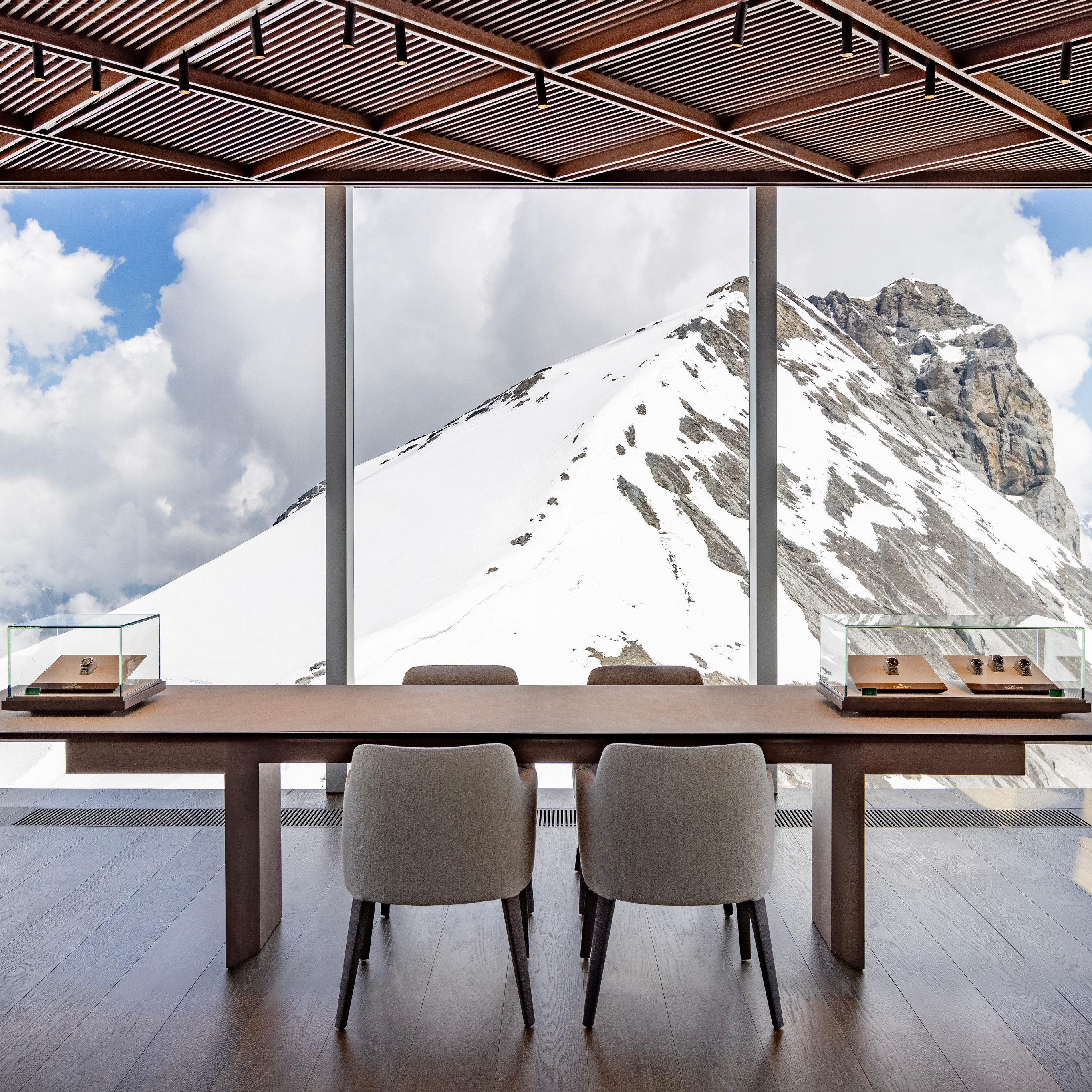 Ein modernes Zimmer mit einem langen Holztisch, Stühlen und Vitrinen, mit Blick auf eine schneebedeckte Bergkette.