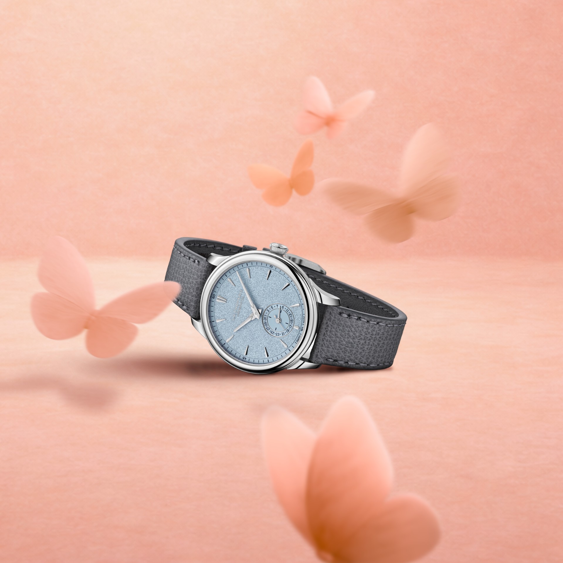 Eine silberne Uhr mit hellblauem Zifferblatt und dunkelgrauem Lederarmband, umgeben von verschwommenen orangefarbenen Schmetterlingen.