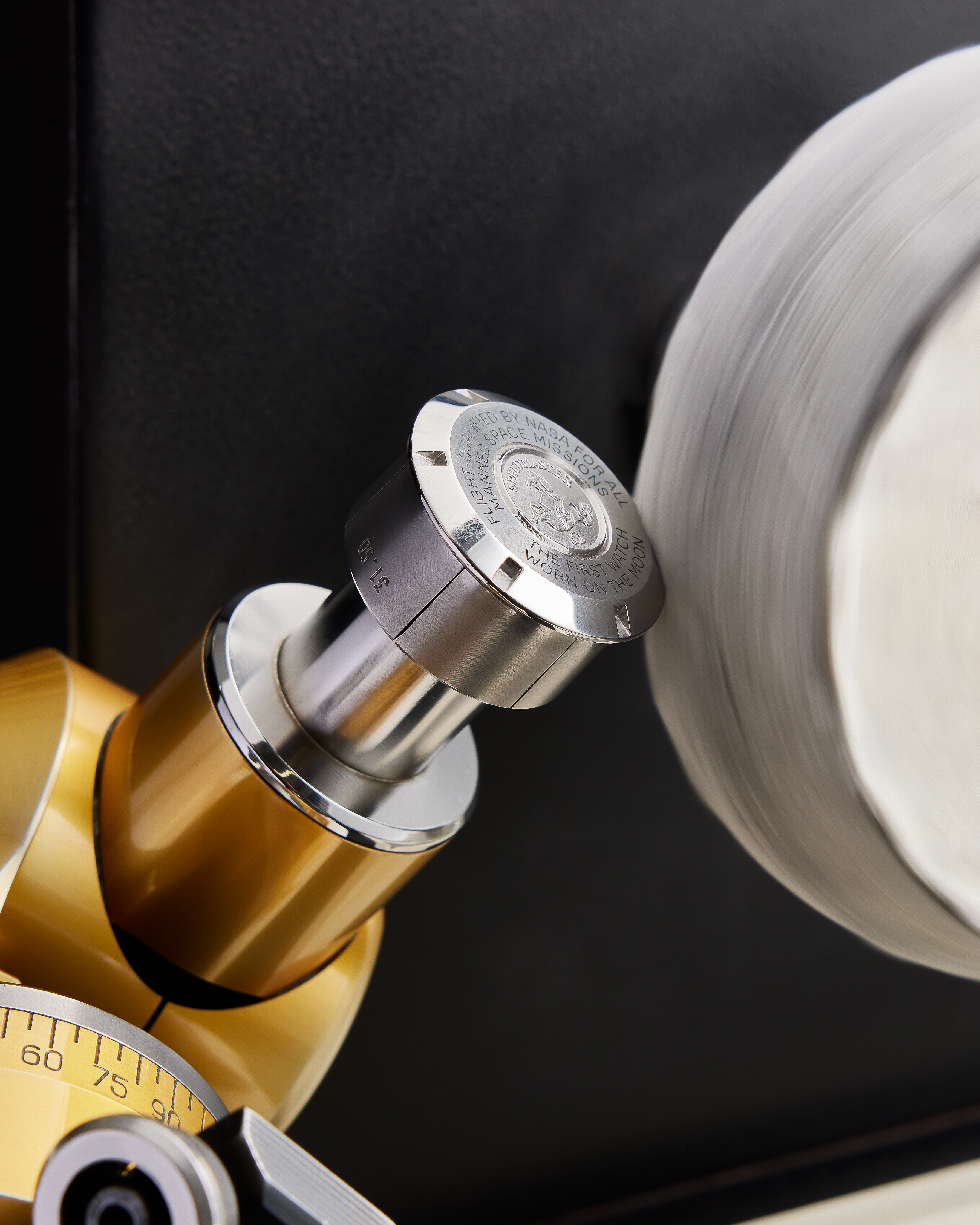 A close-up of a gold and silver watch winder with a spinning white watch face.